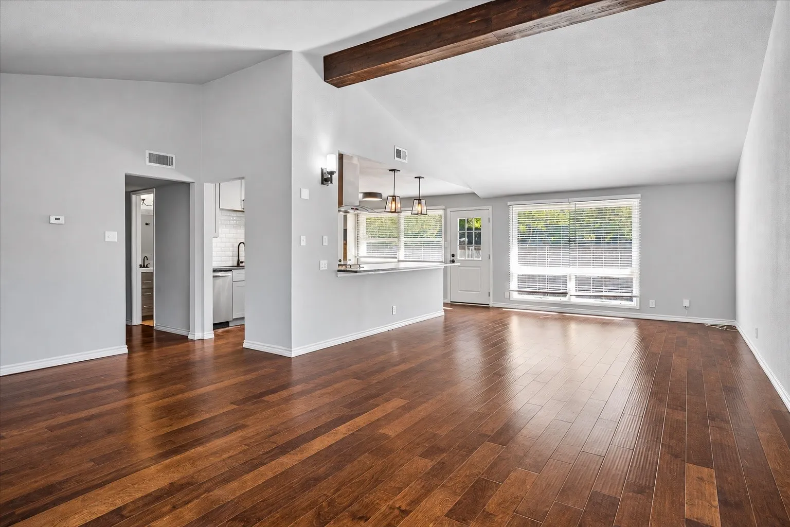 Vaulted ceiling with exposed wood beam, polished wood-finish flooring, and recessed lighting