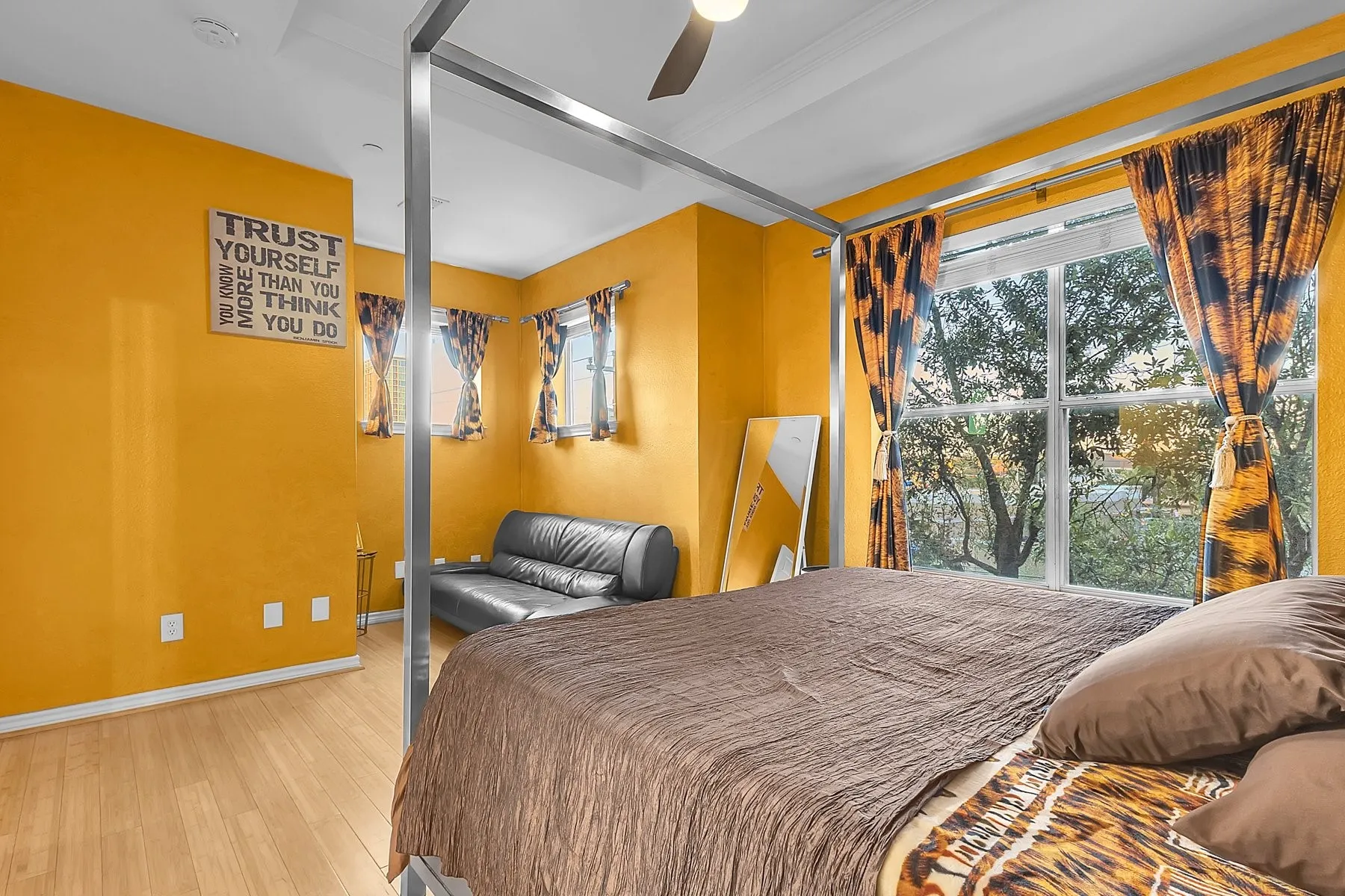 Spacious primary bedroom with tray ceiling, ceiling fan and large window