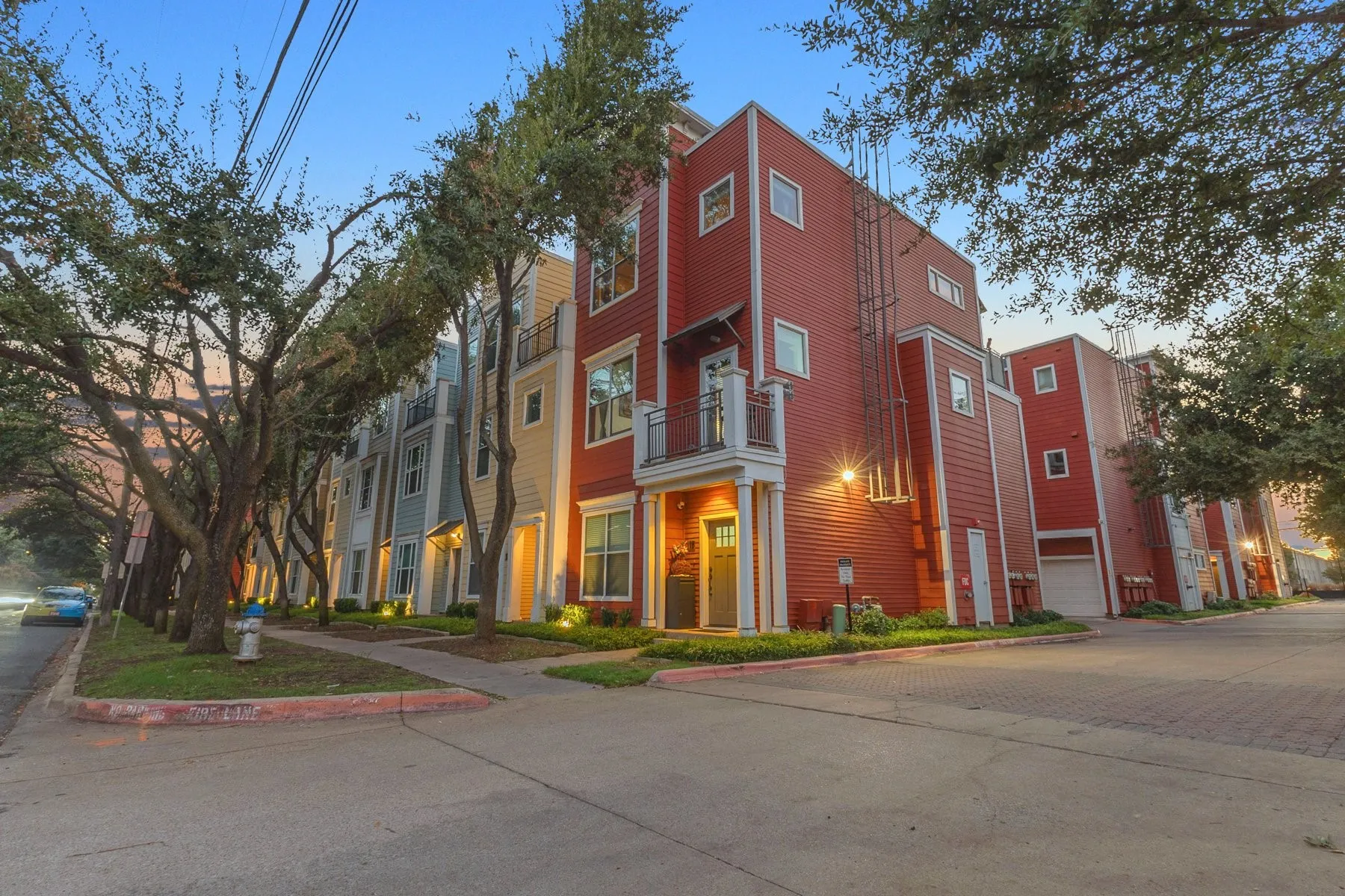 End-unit exterior with mature trees and landscaped beds at dusk