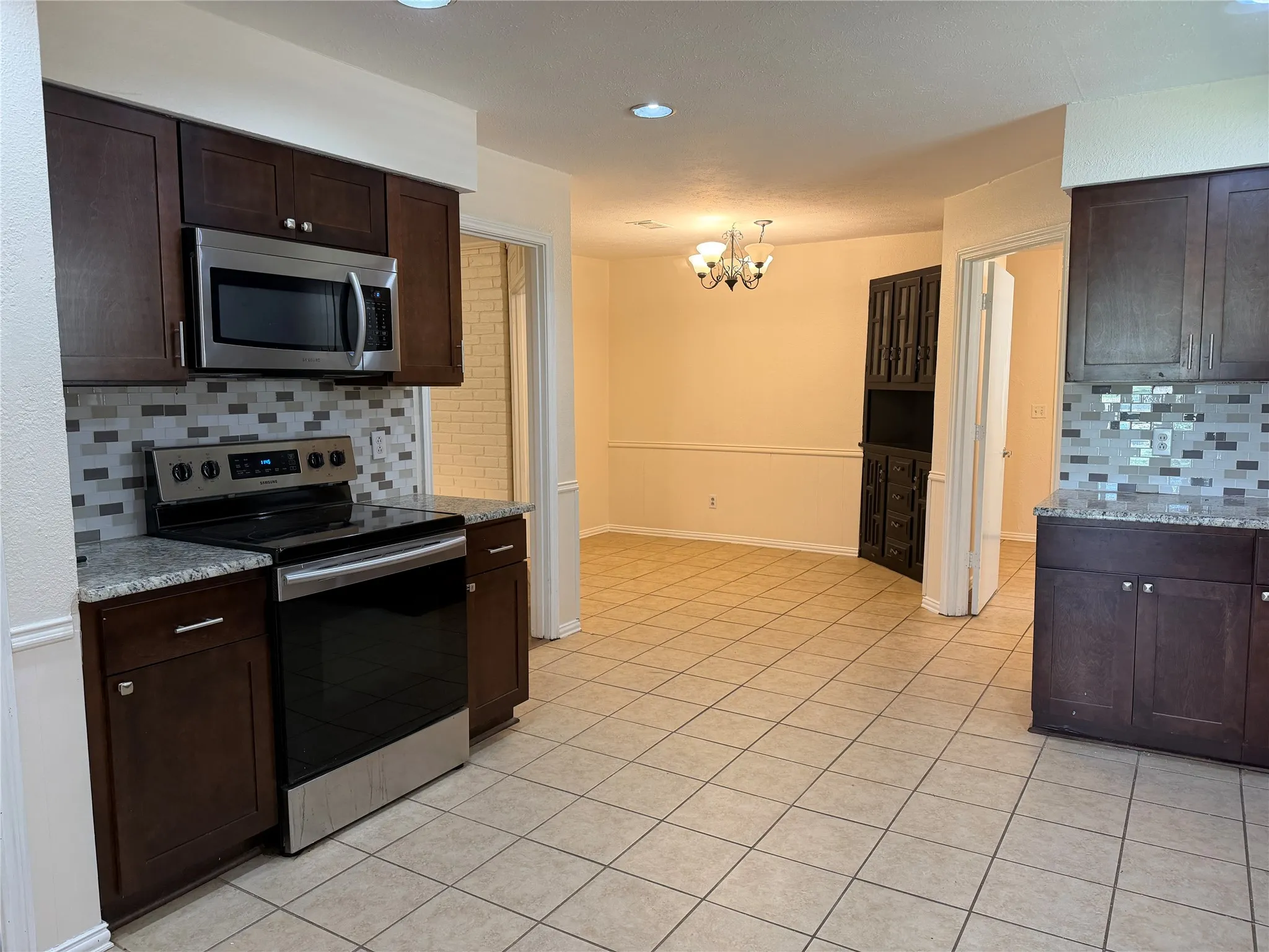 Kitchen with dark wood cabinetry, stainless steel appliances, granite-style countertops, and a tile backsplash