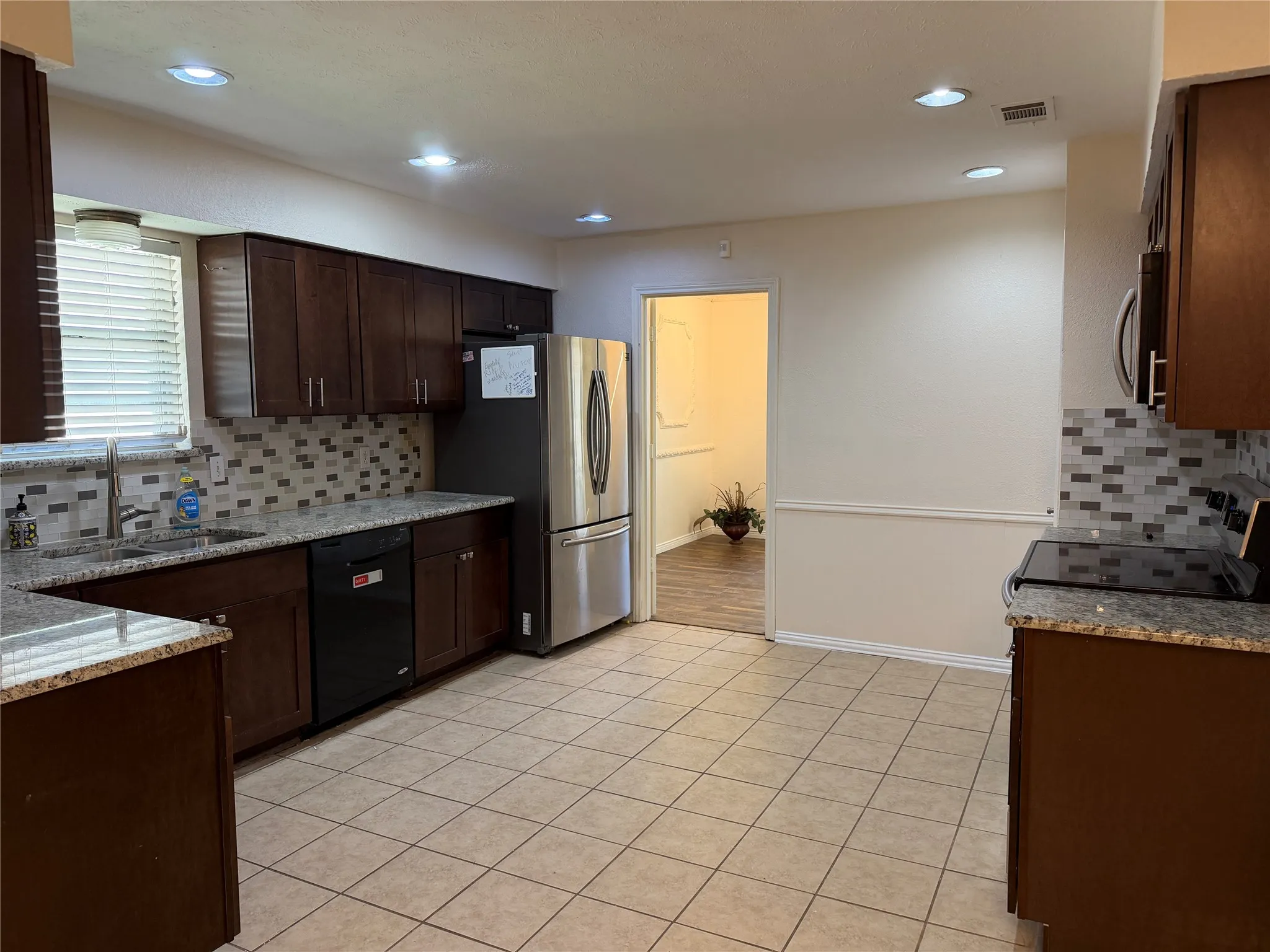 Expansive kitchen featuring dark wood cabinetry, light-colored tile flooring, speckled countertops, a patterned tile backsplash, and recessed lighting