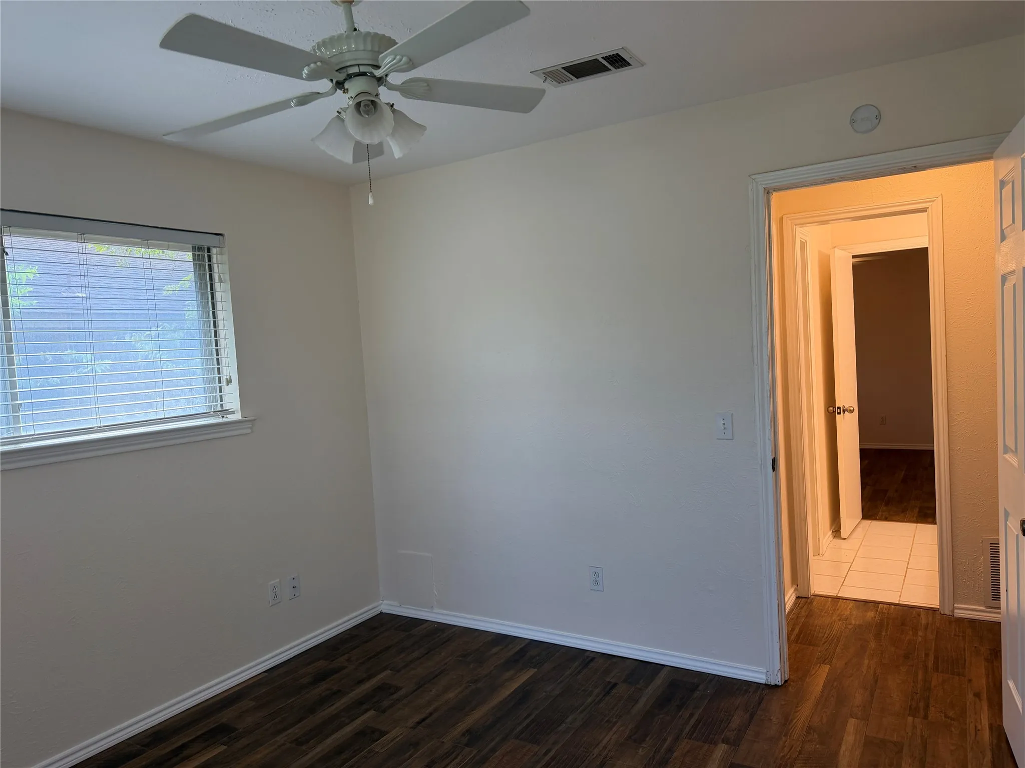 Wood-finish flooring, neutral wall tones, window with blinds, and a ceiling fan with integrated lighting