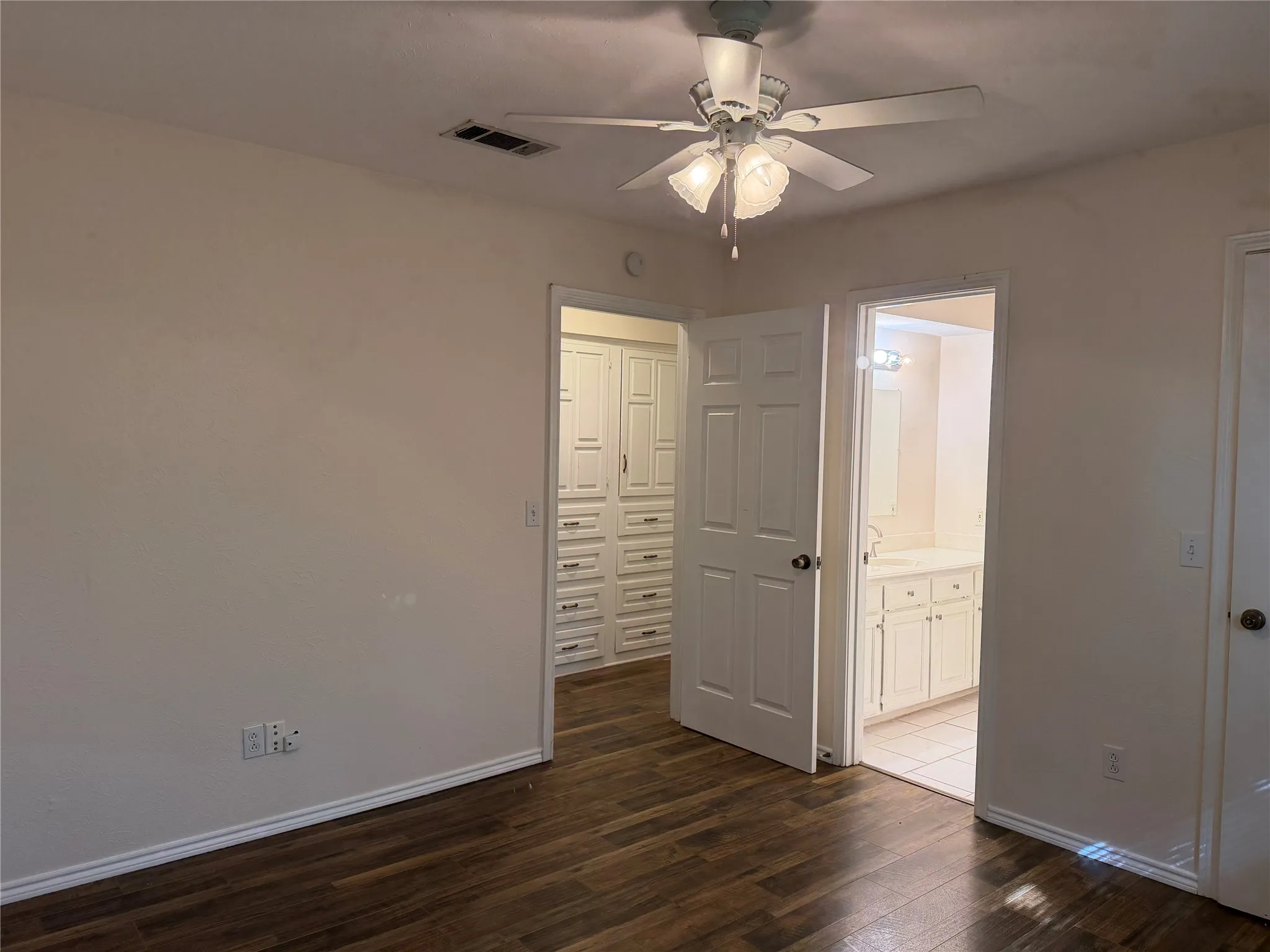Wood-finish flooring with white baseboards, featuring a ceiling fan with light fixture