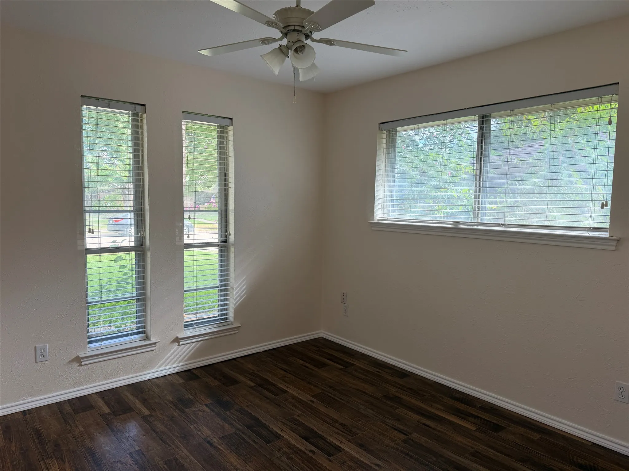 Wood-finish flooring, multiple windows with blinds, and a ceiling fan with integrated lighting
