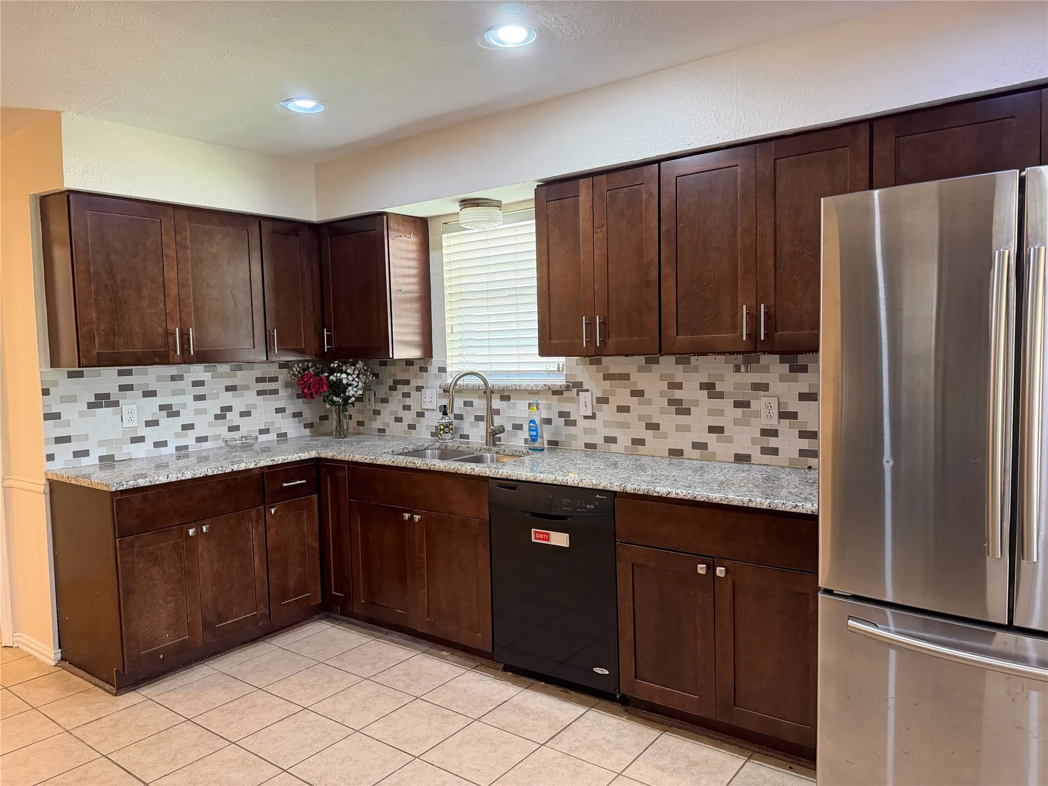 Kitchen featuring dark wood-finish cabinetry, light-toned countertops, a mosaic tile backsplash, stainless steel refrigerator, and recessed lighting
