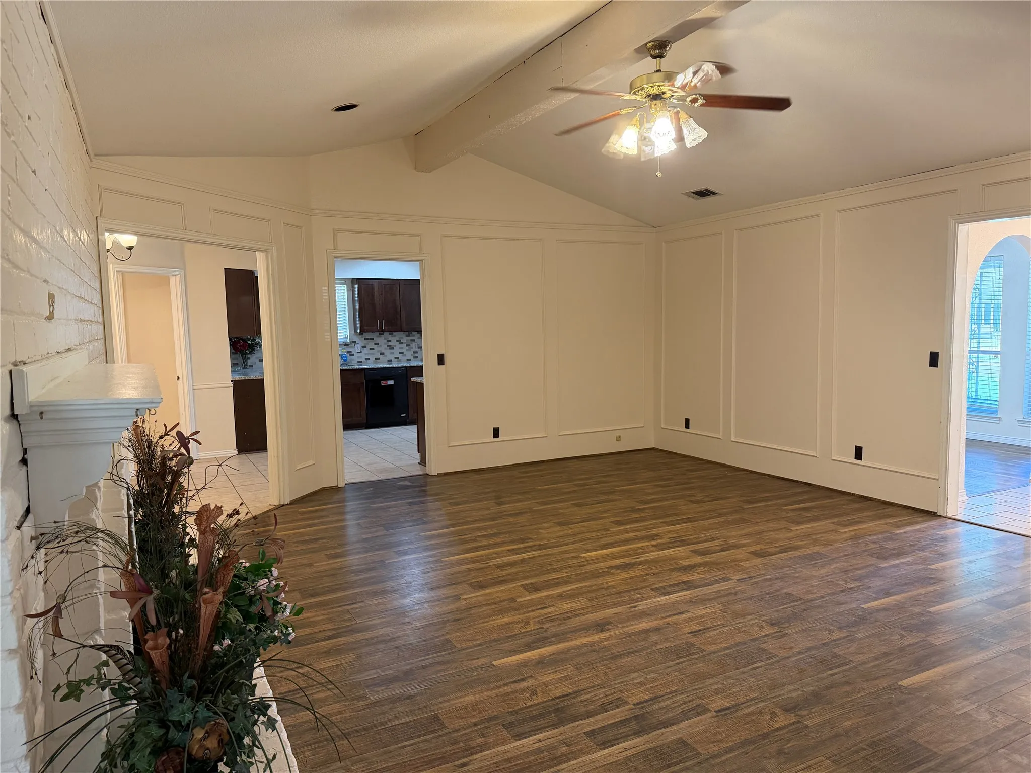 Vaulted ceiling with exposed beam, wood-finish flooring, paneled wall detailing, and a ceiling fan with integrated lighting