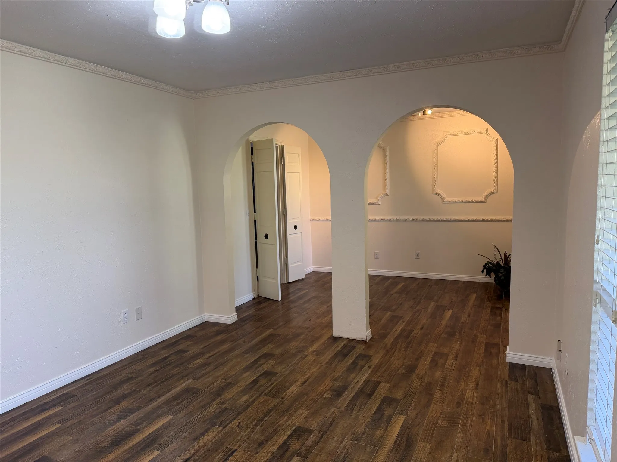 Wood-finish flooring, arched doorways, detailed crown molding, decorative wall trim, and paneled doors