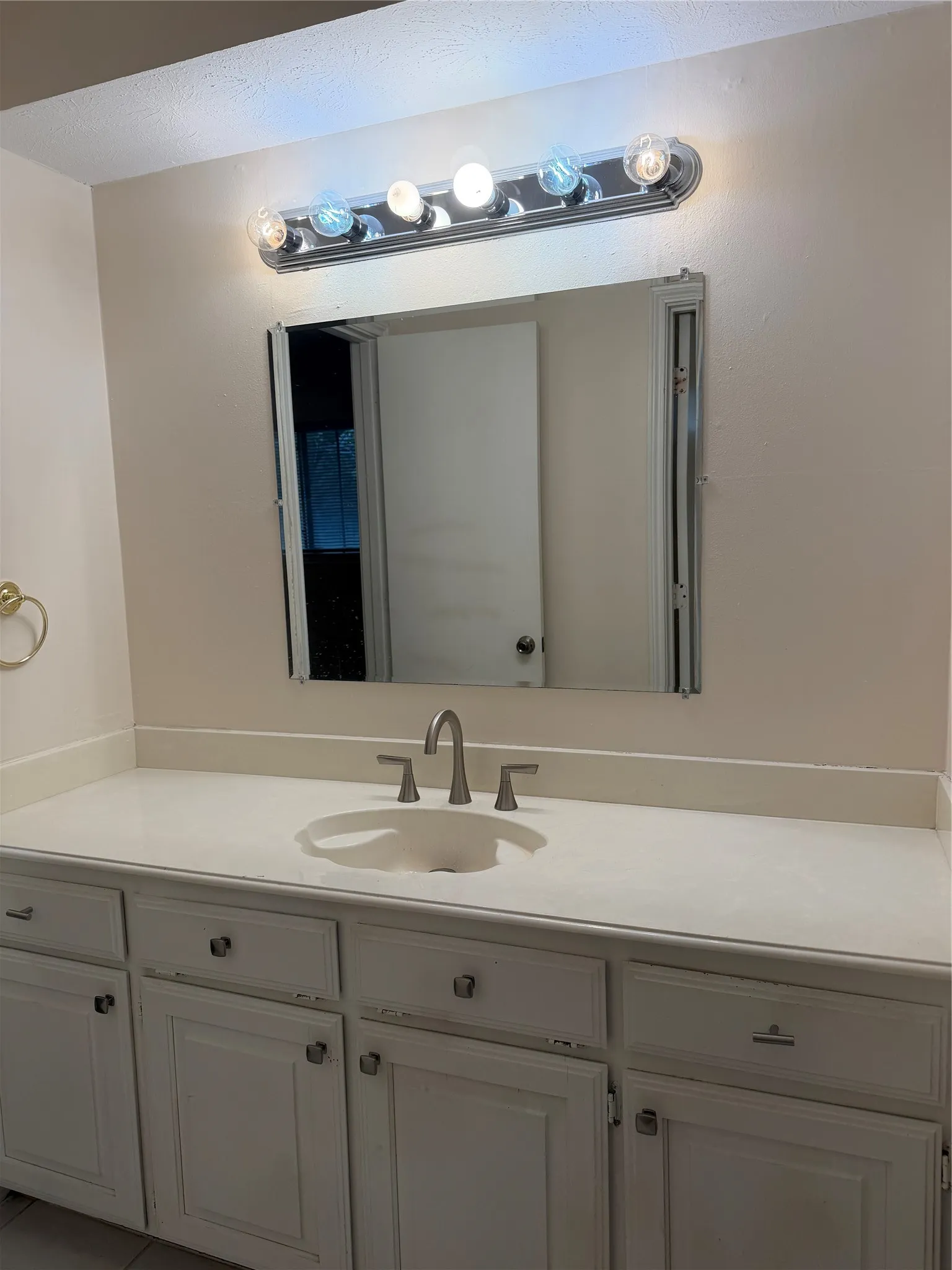 Vanity with white cabinets, light-toned countertop, integrated sink, and brushed nickel faucet