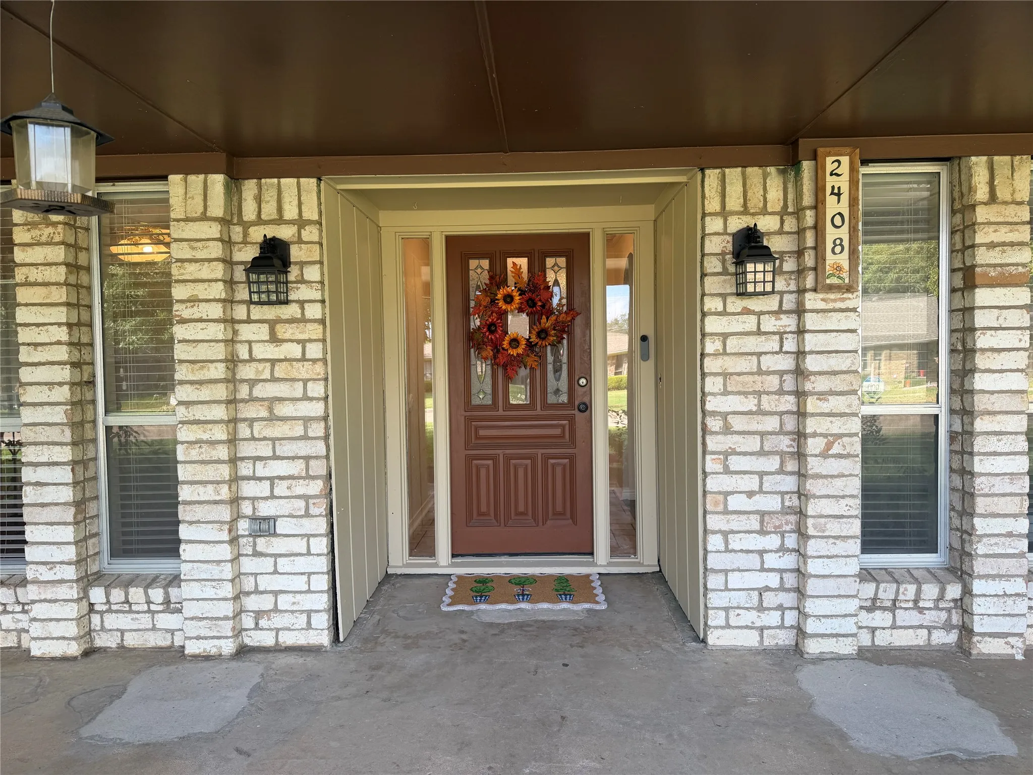 Brick facade with vertical siding accents, decorative entryway with sidelights, and exterior light fixtures
