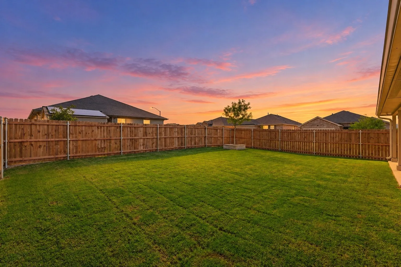 Expansive backyard featuring a manicured lawn, wood privacy fencing, and a built-in planter
