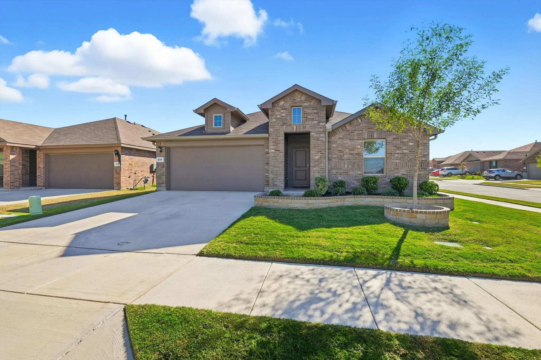 Brick exterior with stone accents, attached two-car garage, concrete driveway, front yard landscaping, and a street-facing entryway