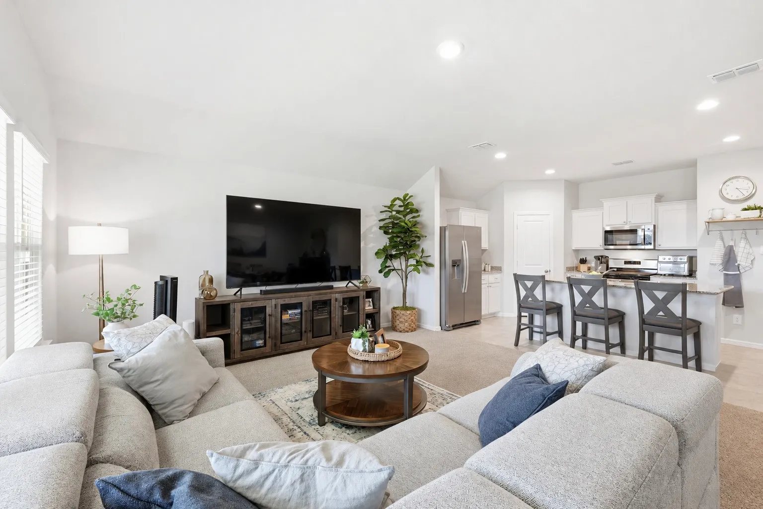 Recessed lighting, wood-finish media console, stainless steel appliances, kitchen island with seating, and white cabinetry