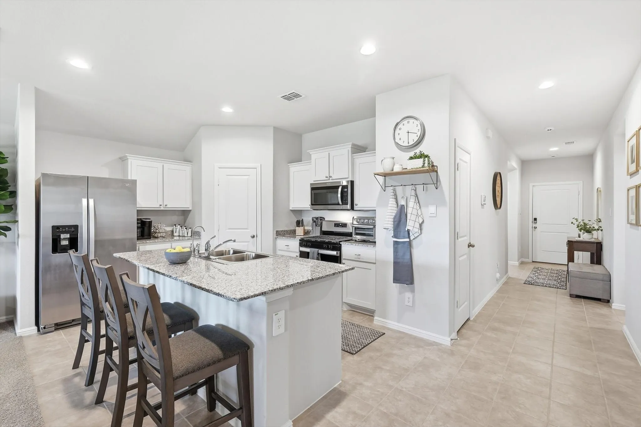White cabinetry with stainless steel appliances, central island with granite countertop and double basin sink, and recessed lighting