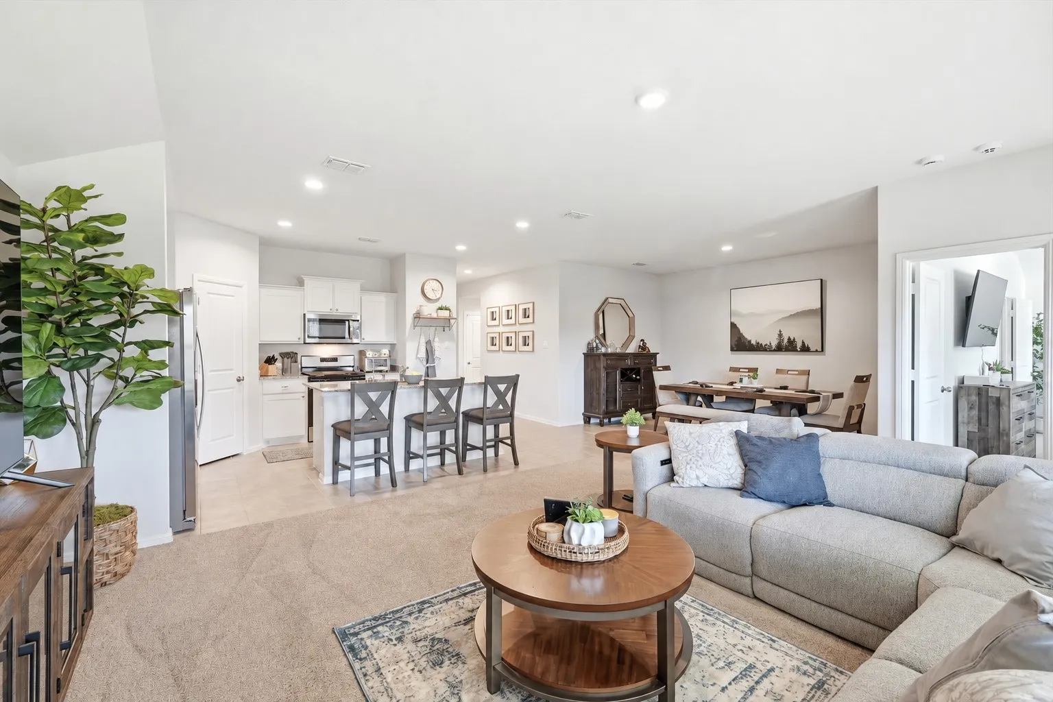 Open-concept living space with recessed lighting, carpeted area, and an adjacent kitchen featuring a breakfast bar with seating