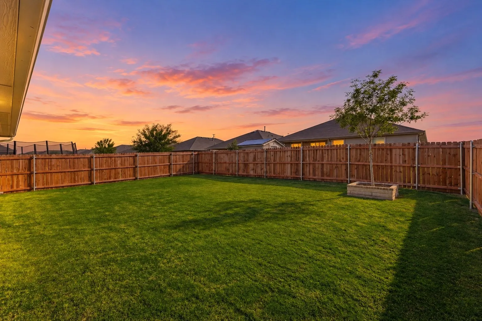 Expansive backyard featuring a manicured lawn, full perimeter wood fencing, and a decorative tree planter