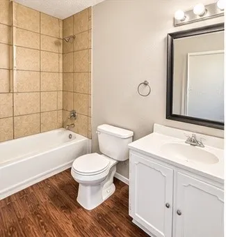 Wood-finish flooring, white vanity with cabinet storage, framed mirror, and tiled shower surround