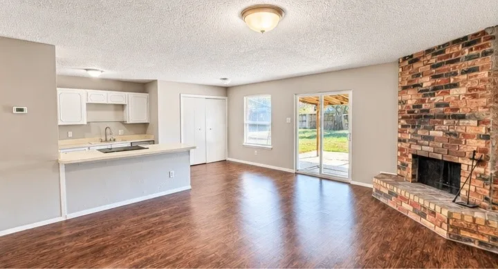 Wood-finish flooring throughout, brick fireplace with hearth, white cabinetry, light countertops, and sliding glass doors to the exterior