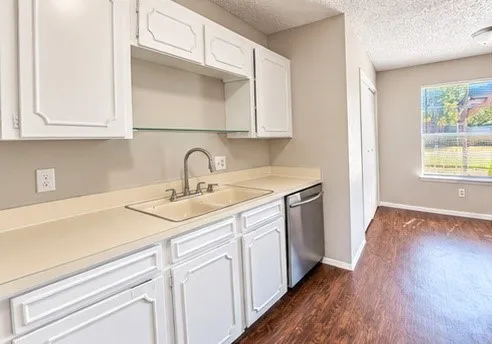 Kitchenette featuring white cabinetry, a double basin sink with a gooseneck faucet, light-toned countertops, and a stainless steel dishwasher