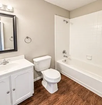 Bathroom featuring a white vanity with integrated sink, wood-finish flooring, and a white tiled shower/tub combination