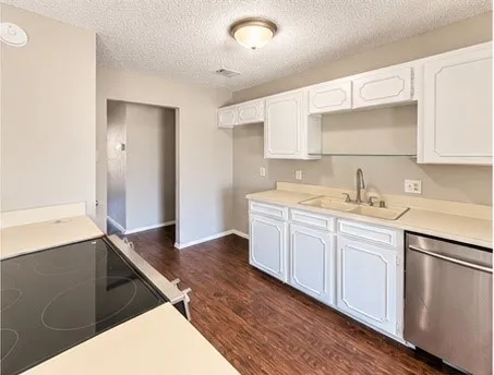 Kitchen featuring white cabinetry, light-toned countertops, wood-finish flooring, a stainless steel dishwasher, and a built-in electric cooktop