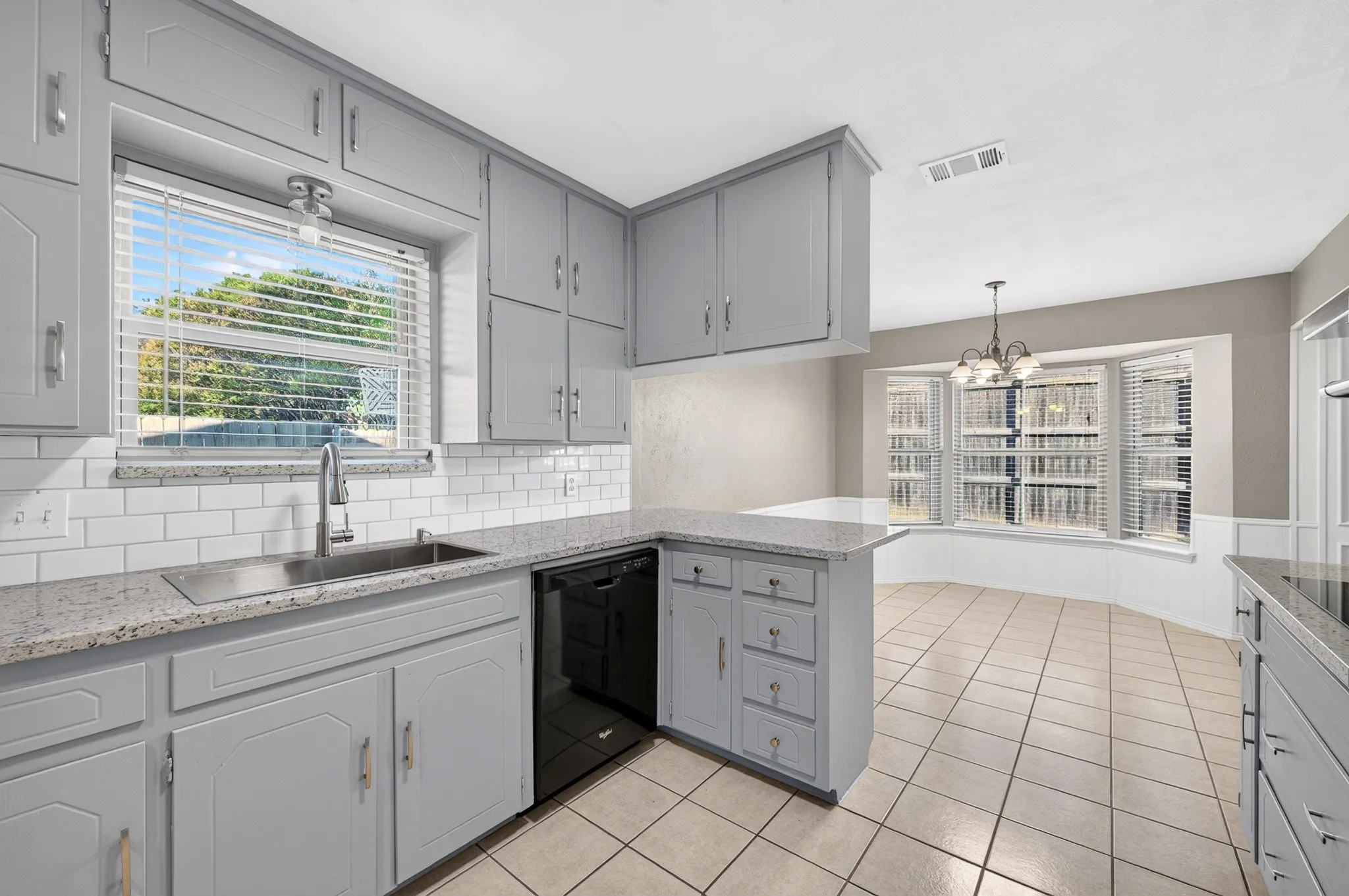 Light gray cabinetry with brushed nickel hardware, white subway tile backsplash, light granite-style countertops, stainless steel sink with gooseneck faucet, and tiled flooring
