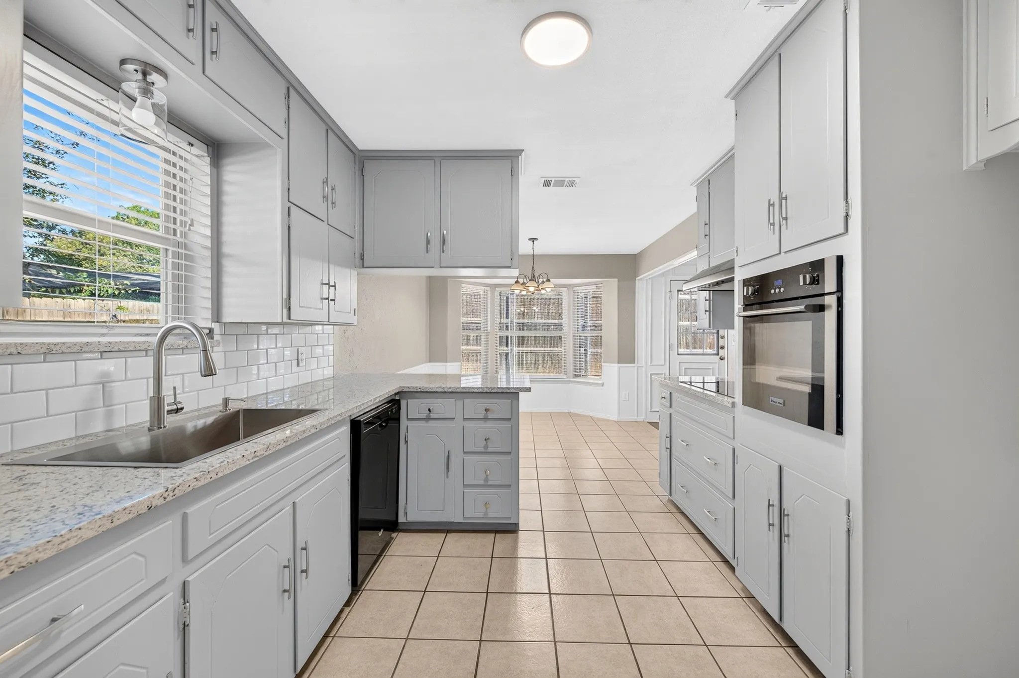 Kitchen featuring a stainless steel sink, subway tile backsplash, light-colored countertops, built-in oven, and tile flooring