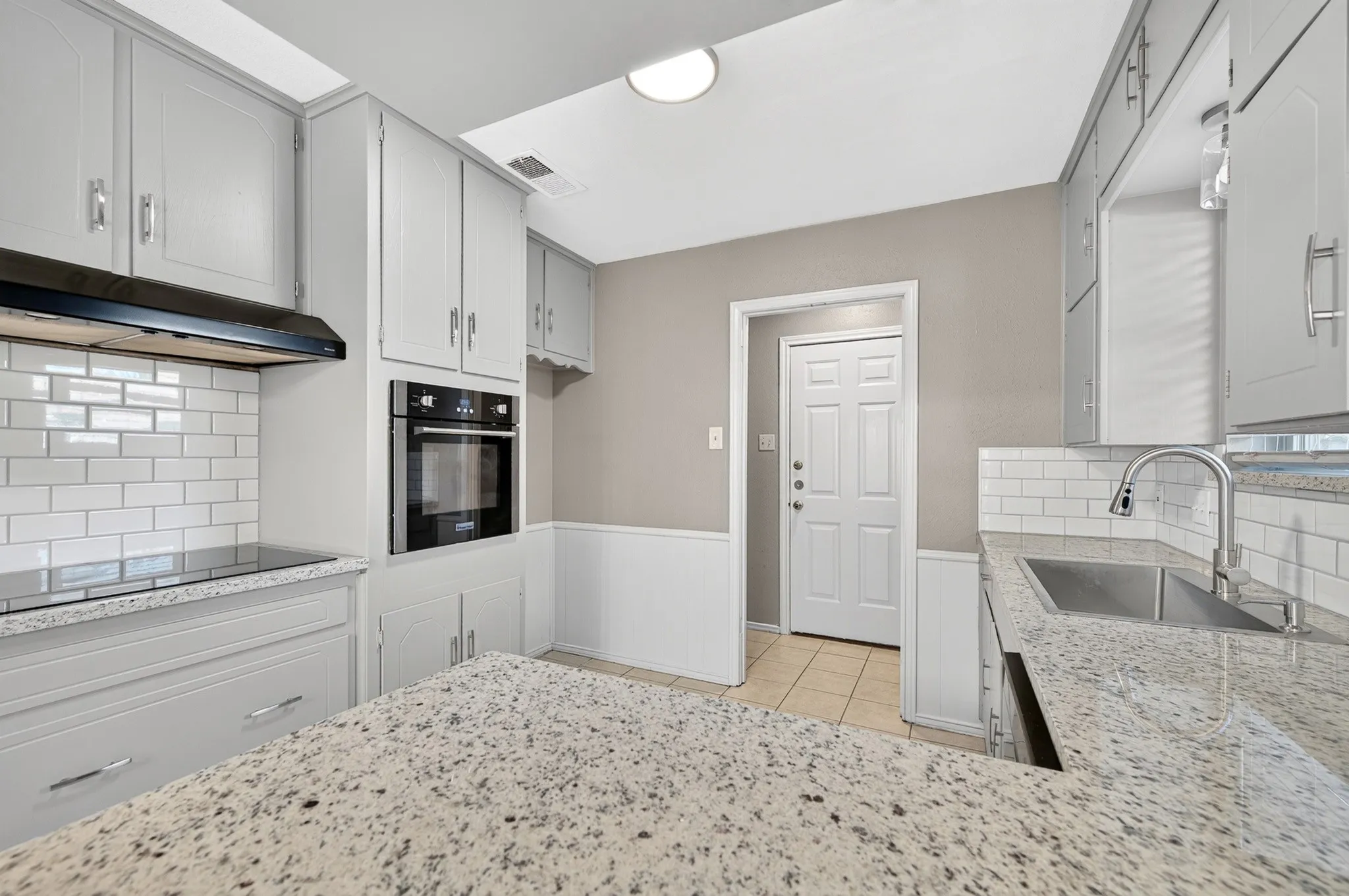 Granite countertops, white subway tile backsplash, stainless steel double basin sink, and built-in wall oven