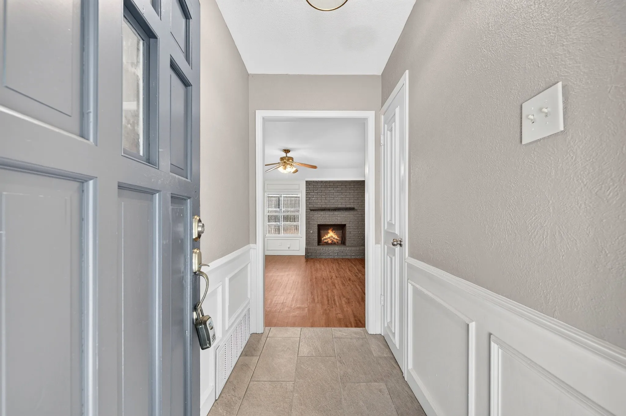 Panel-style front door with glass inserts, tile flooring, and wainscoting details