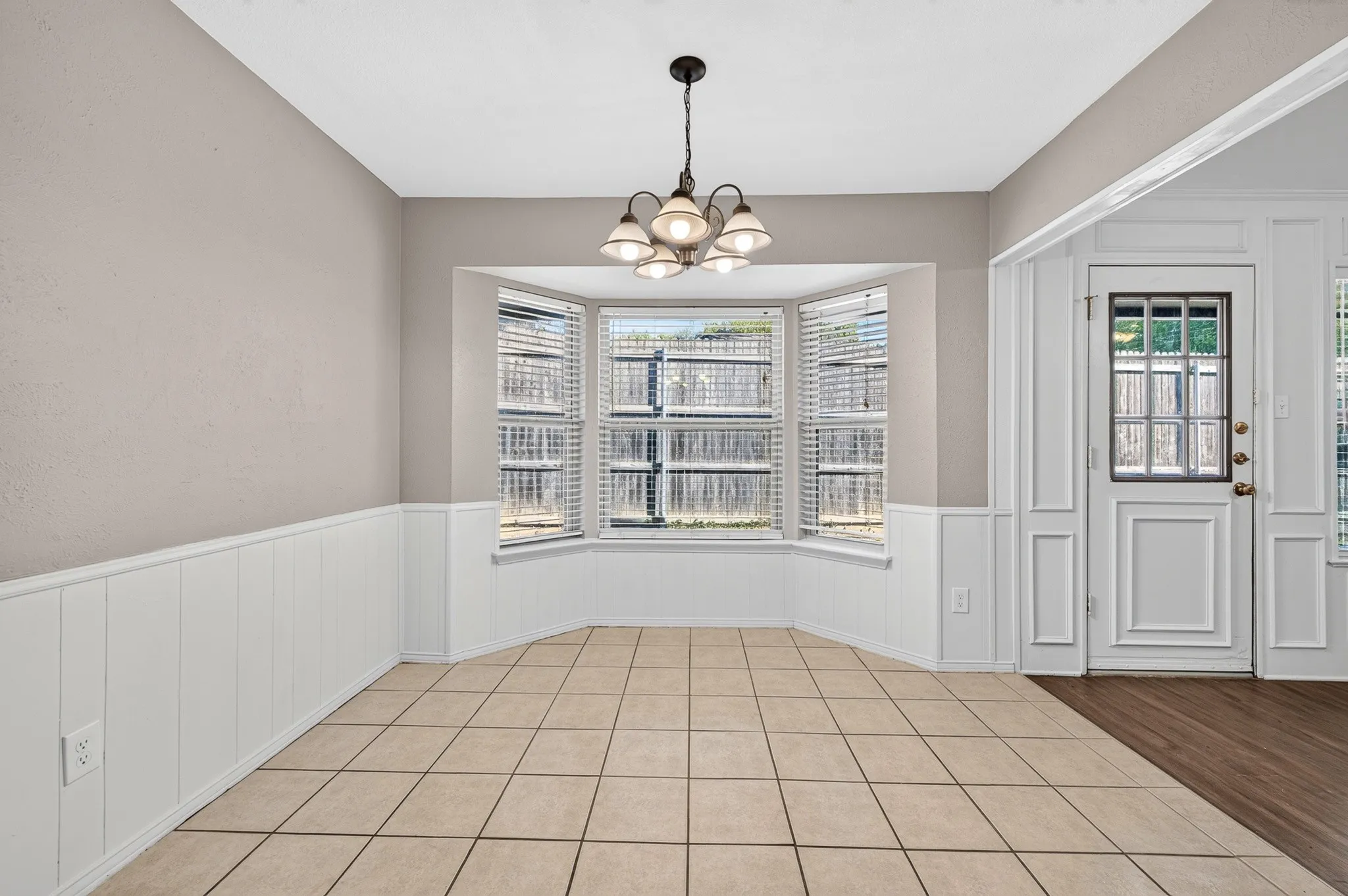 Bay window with blinds, tile flooring, recessed lighting, and wainscoting