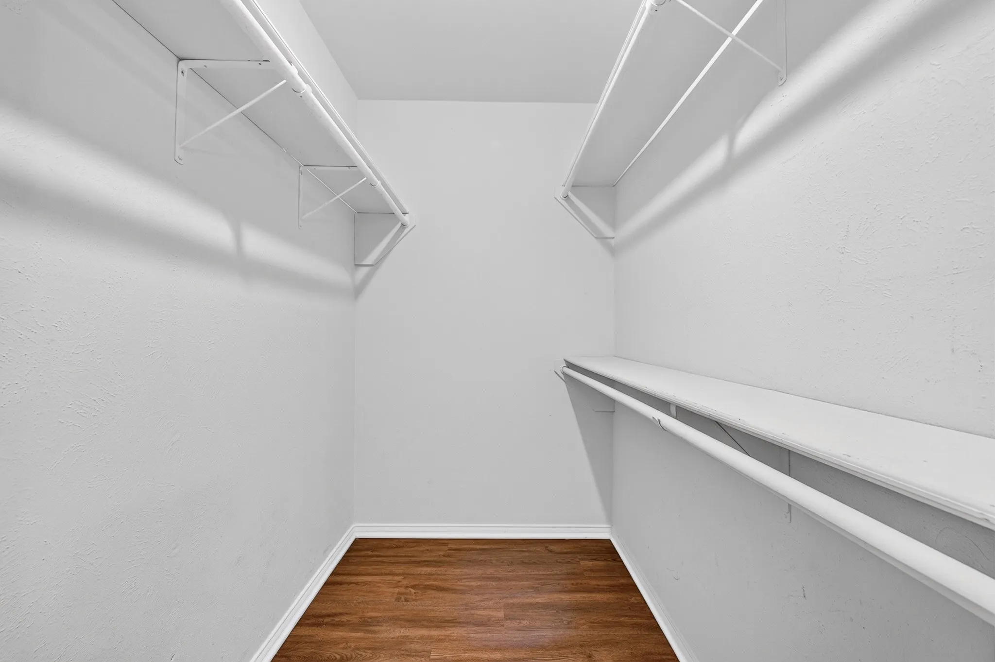 Walk-in closet featuring wood-finish flooring, white walls, and built-in shelving with hanging rods