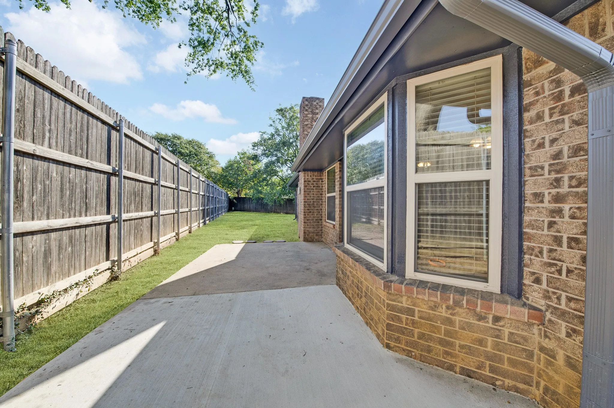 Brick exterior with white-framed windows, concrete patio, and fenced yard