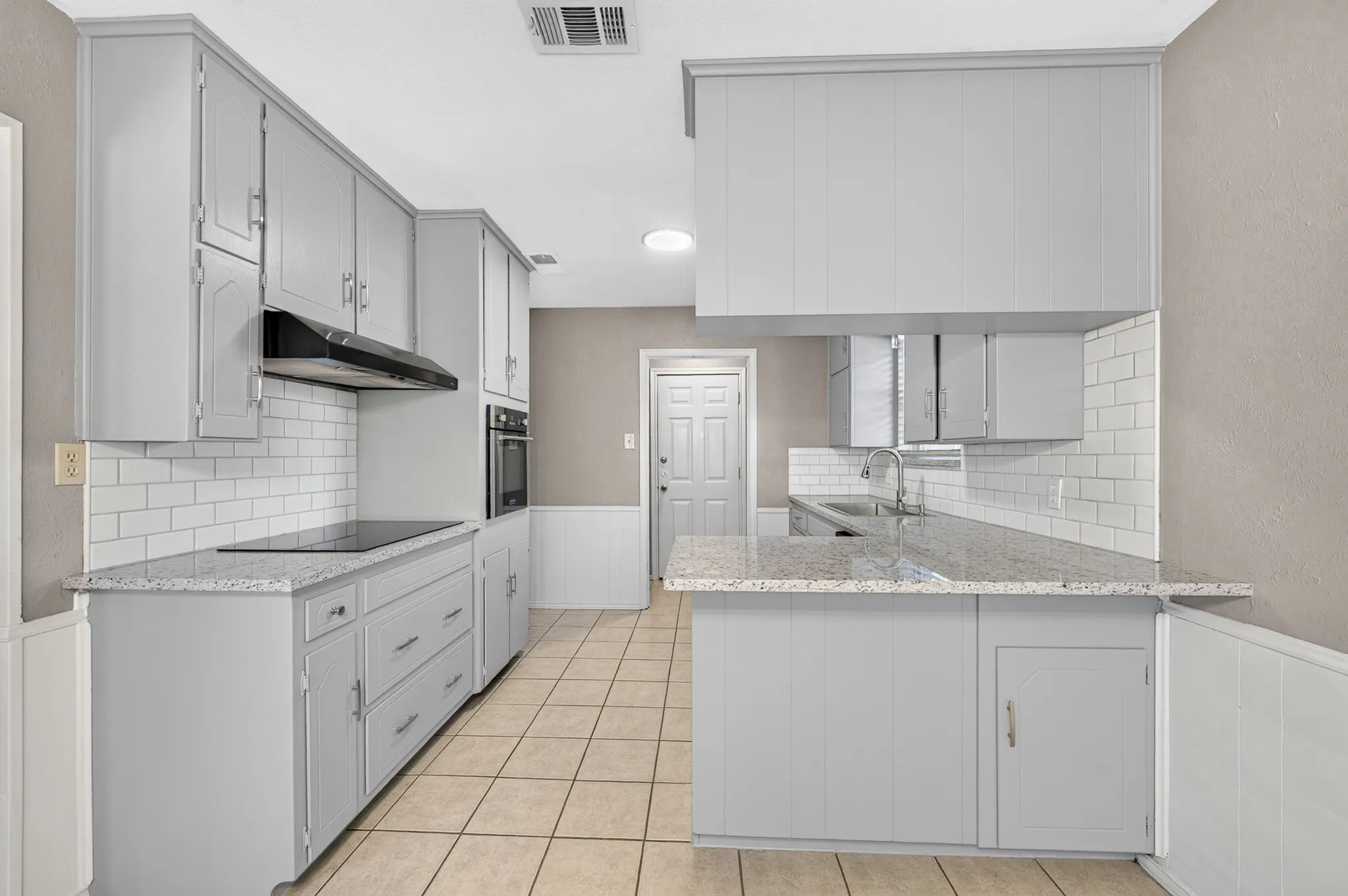Kitchen featuring gray cabinetry, light-toned countertops, white subway tile backsplash, and tile flooring