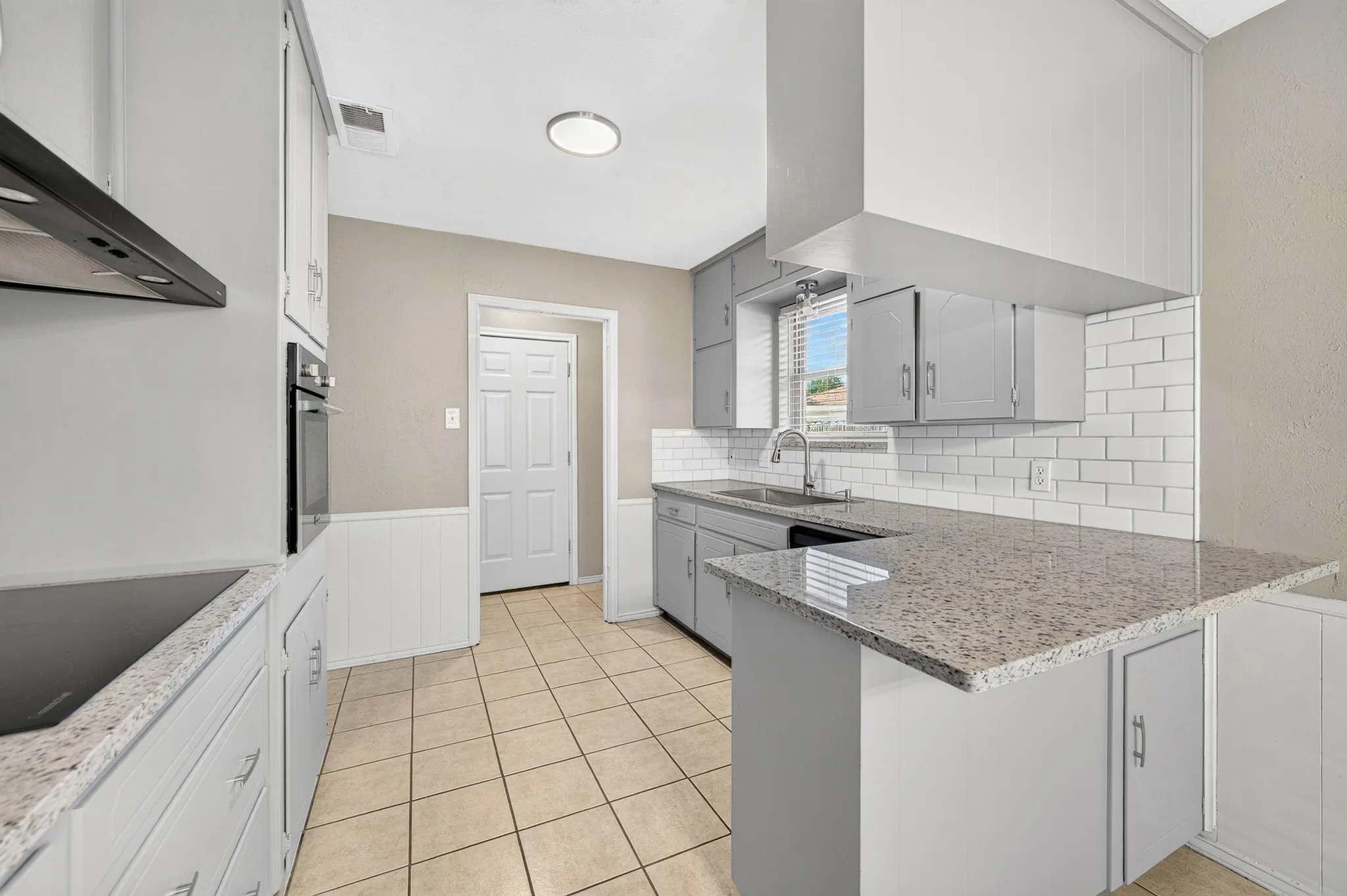 Galley kitchen featuring light gray cabinetry, built-in oven, solid surface countertops, subway tile backsplash, and tile flooring