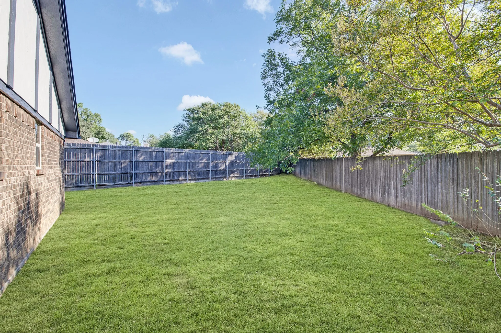 Expansive fenced backyard featuring a manicured lawn, mature trees, and a brick exterior