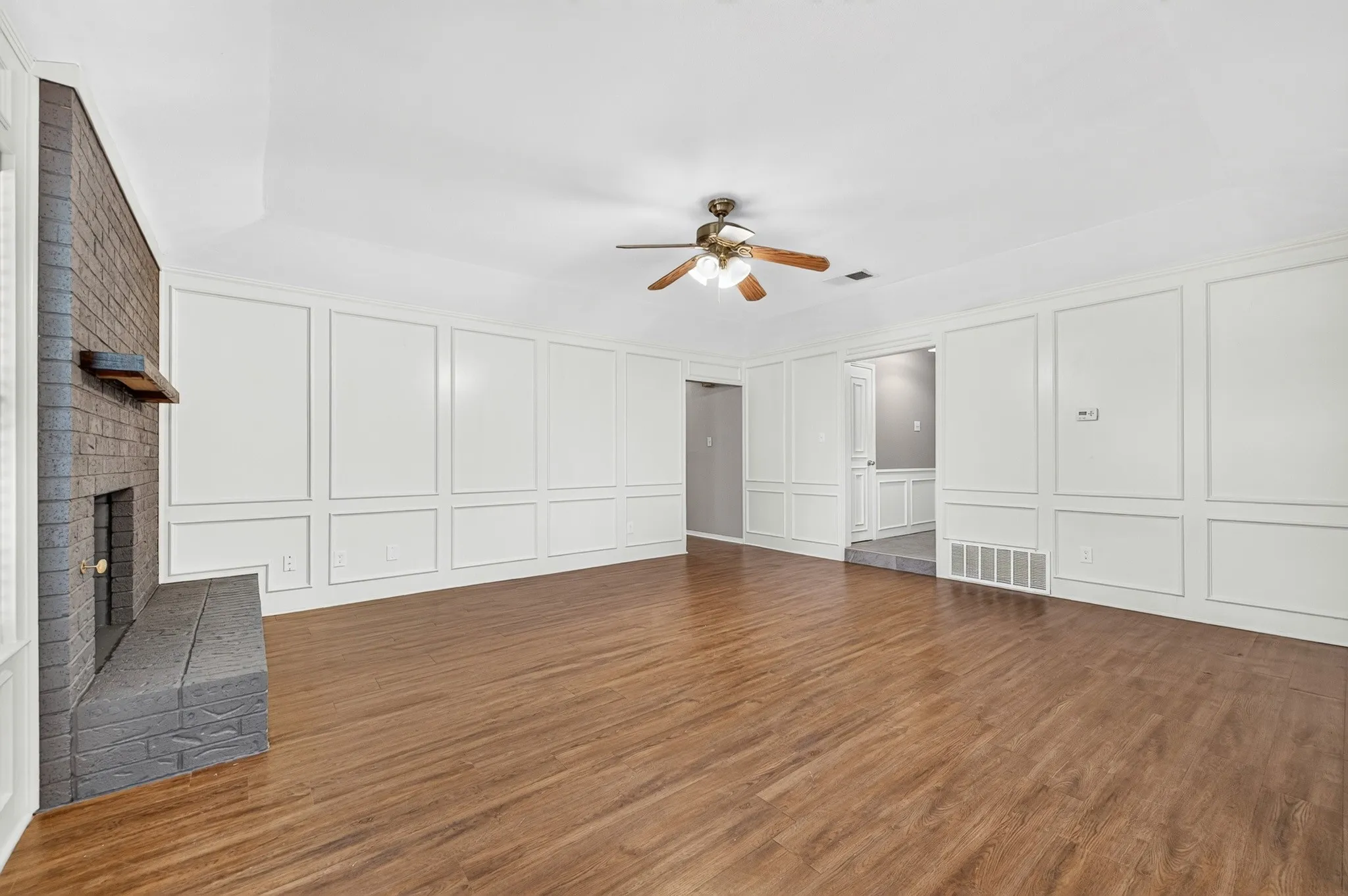 Spacious room with wood-finish flooring, a brick fireplace, and extensive wall paneling