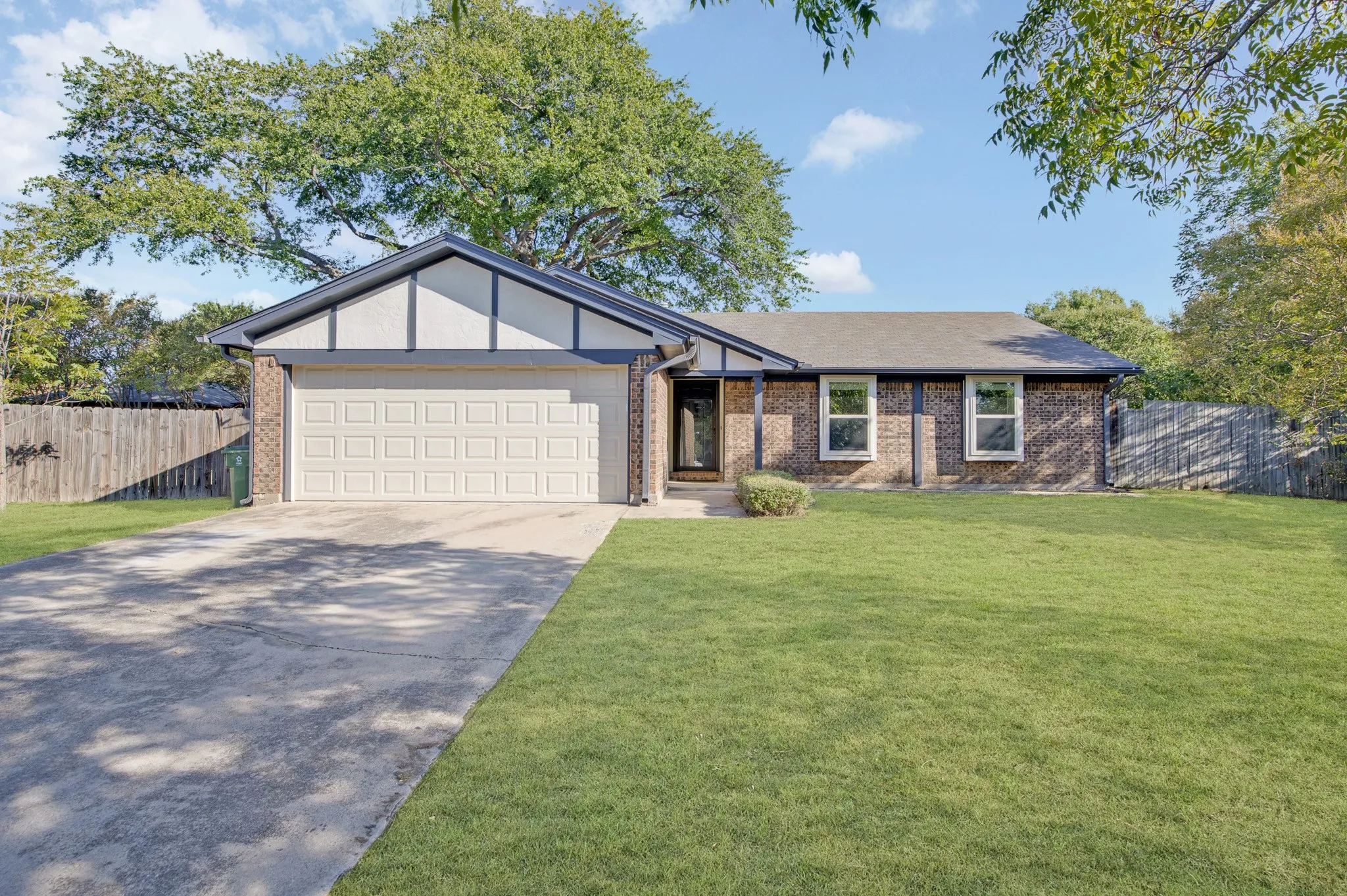 Brick exterior with white trim details, an attached garage, a concrete driveway, and a fenced perimeter