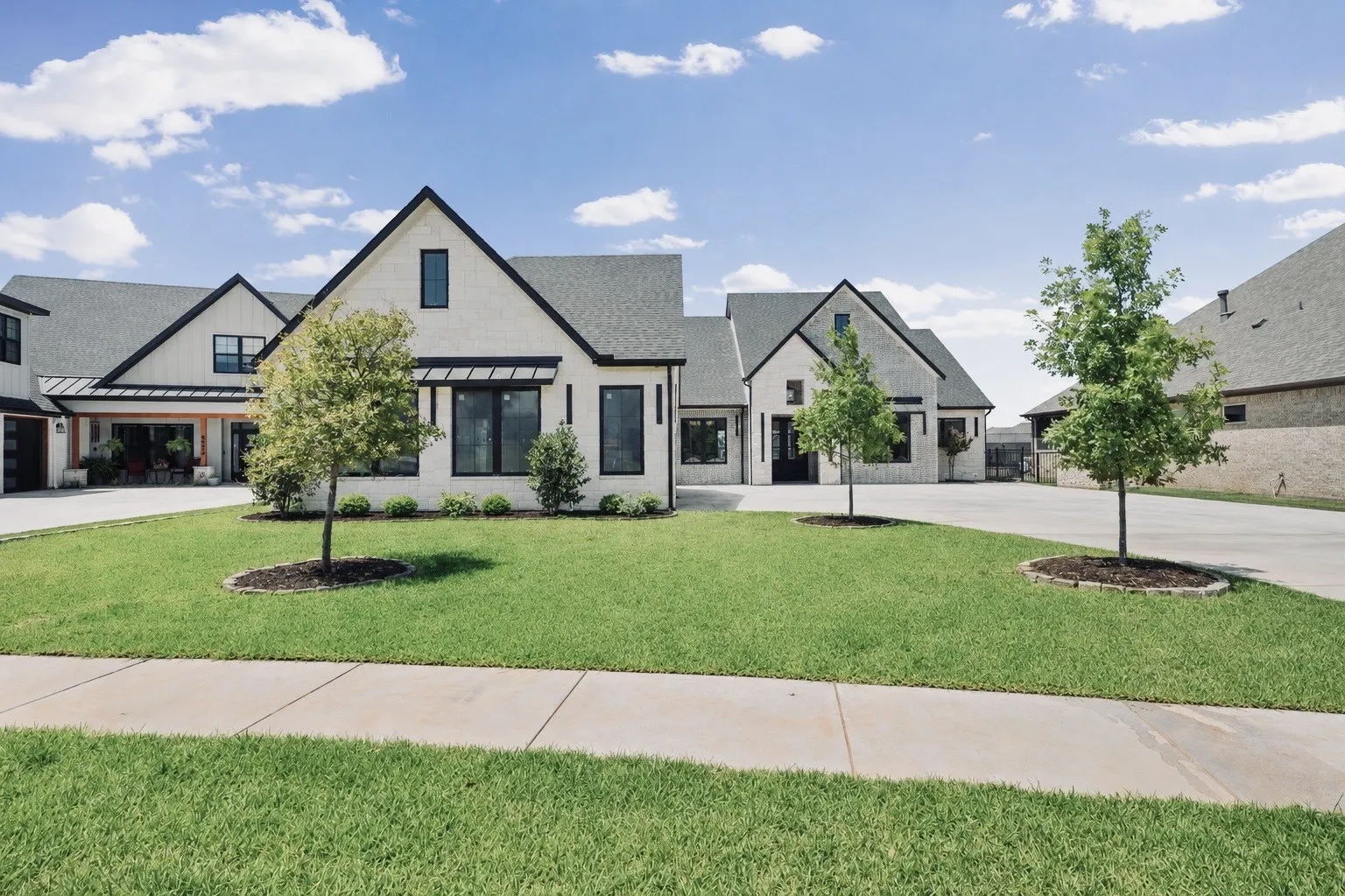 Contemporary farmhouse-style exterior featuring a white brick facade, black-framed windows, and a covered front entry