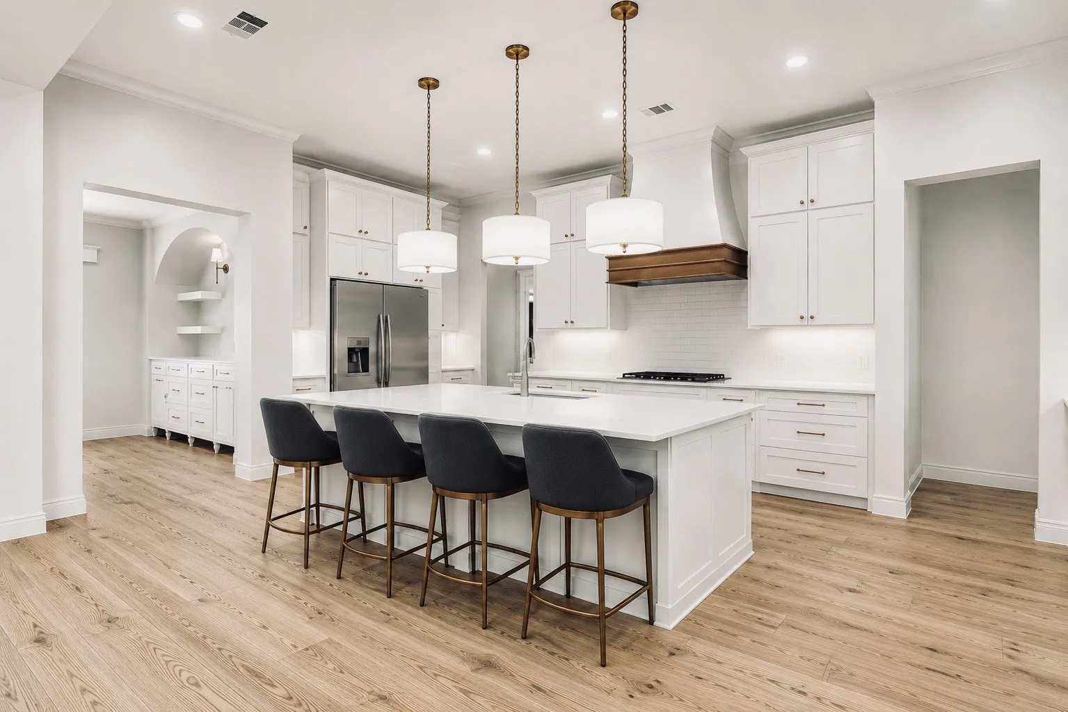 Gourmet kitchen featuring a substantial island, wood-finish flooring, stainless steel appliances, white cabinetry, and pendant lighting