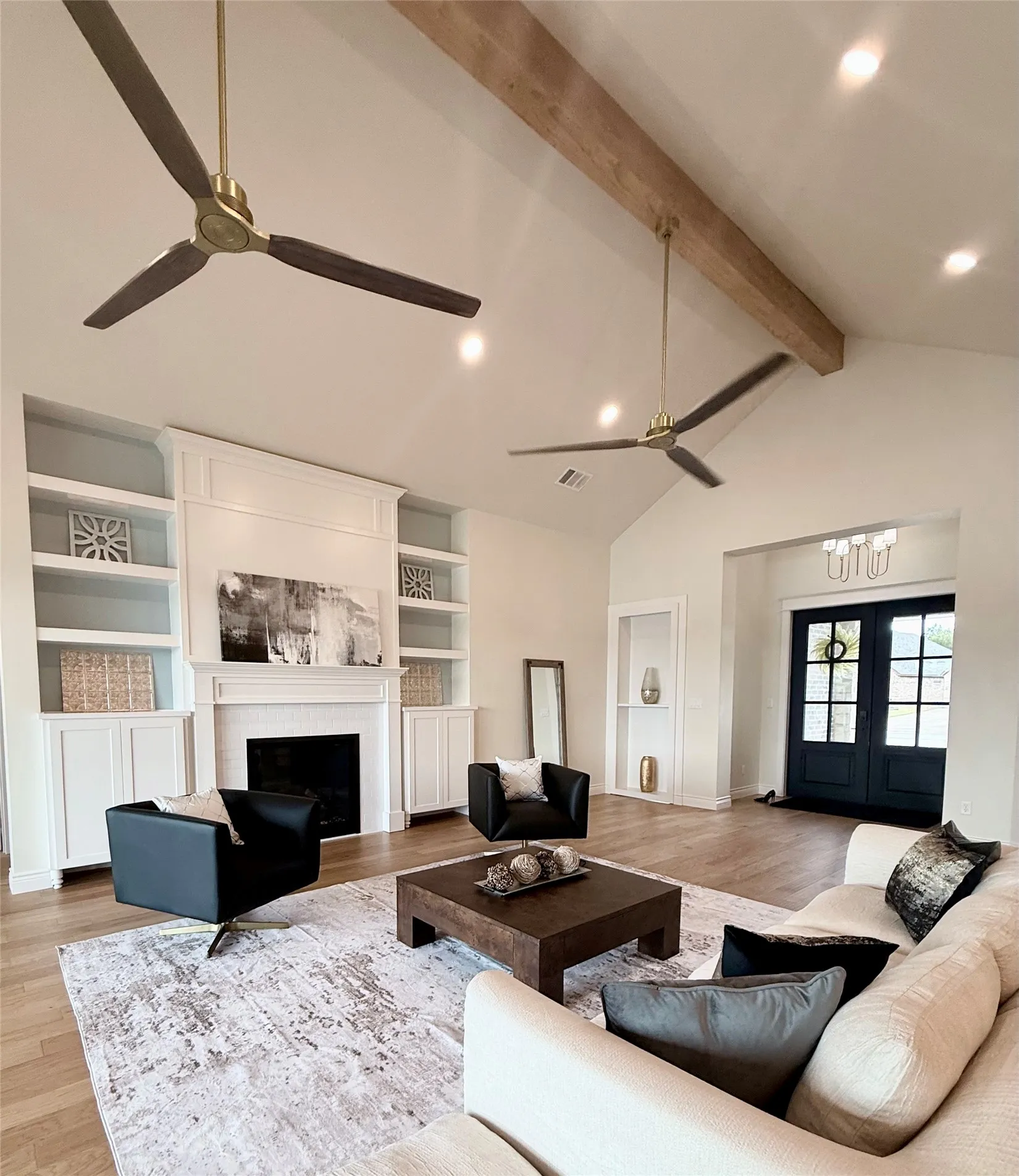 Vaulted ceiling with exposed wood beam, recessed lighting, hardwood flooring, built-in shelving, and a prominent fireplace with a mantel