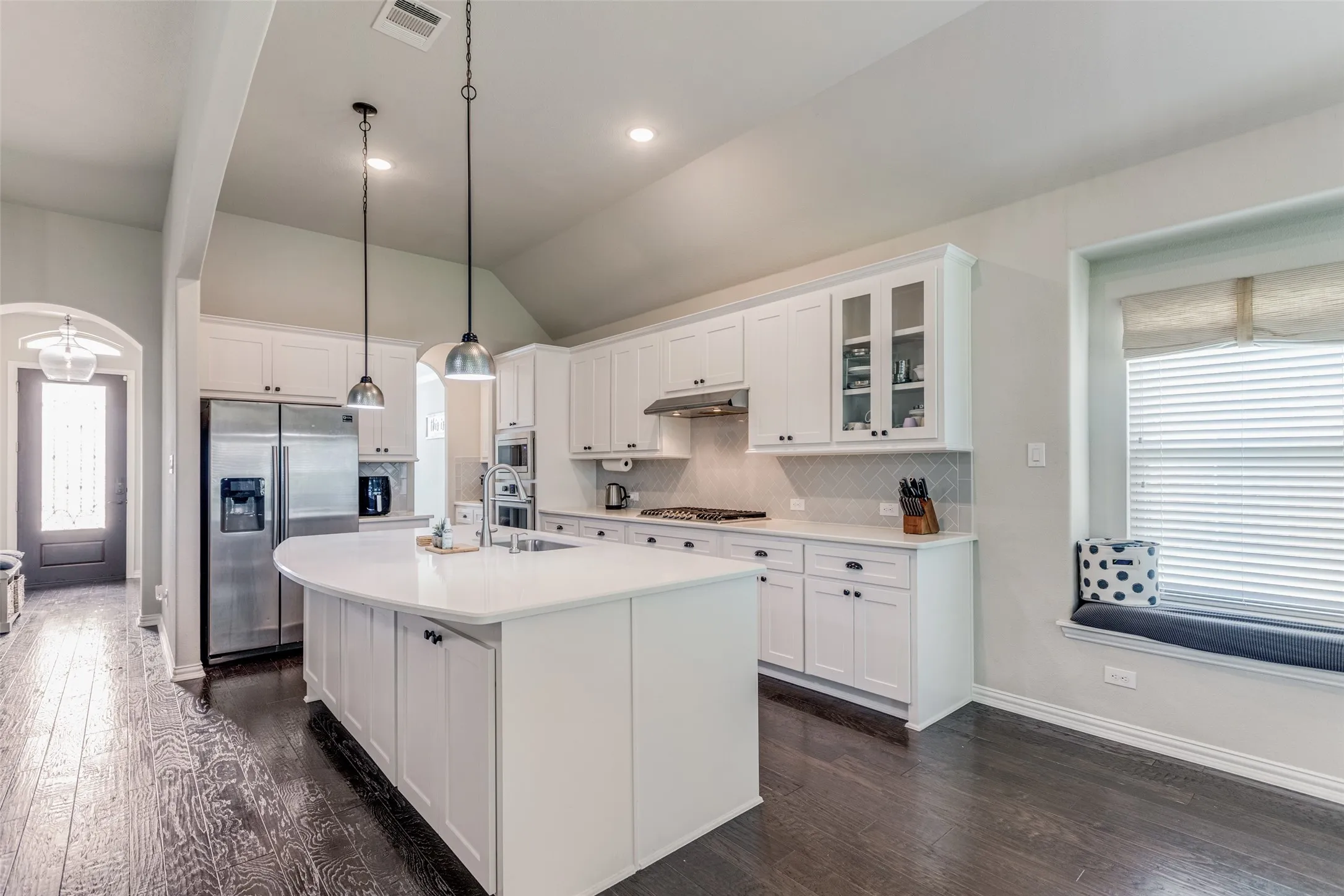 Kitchen featuring white cabinetry, a curved island with integrated sink, stainless steel appliances, and a window seat