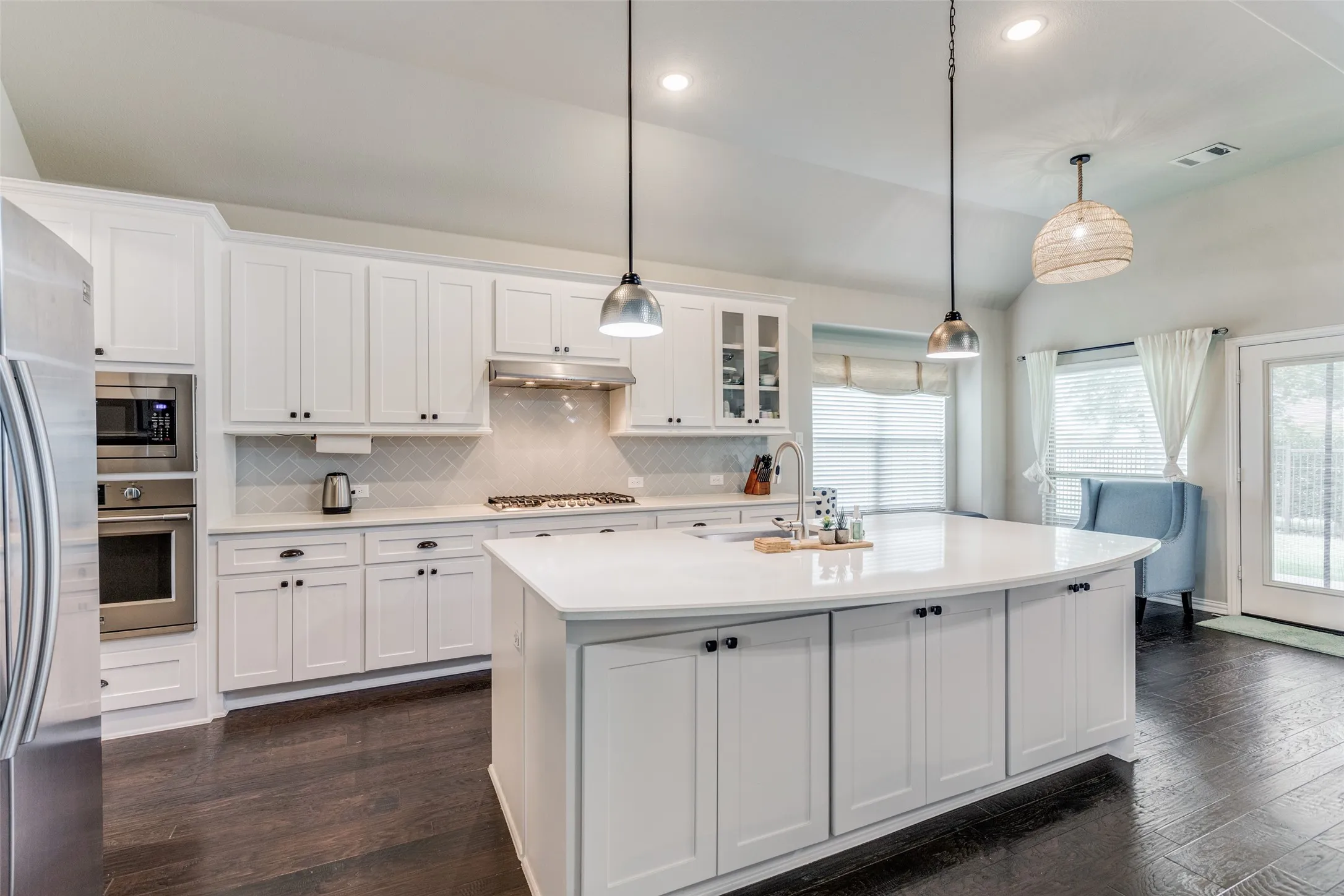 Bright kitchen featuring white cabinetry, a large center island, stainless steel appliances, and dark wood-finish flooring
