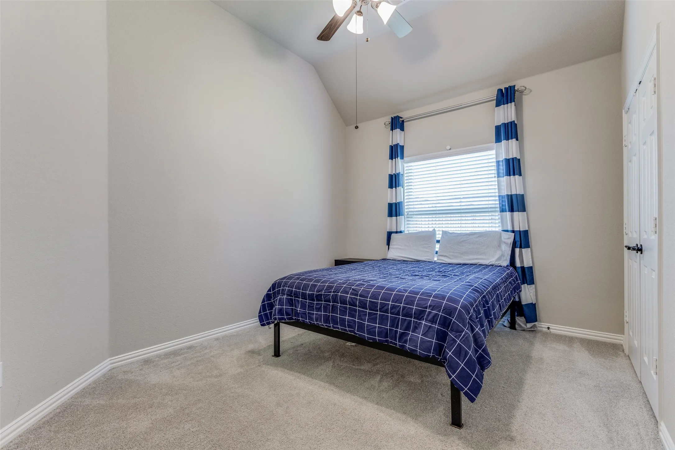 Vaulted ceiling, ceiling fan, window with blinds, light gray wall paint, and light gray carpet