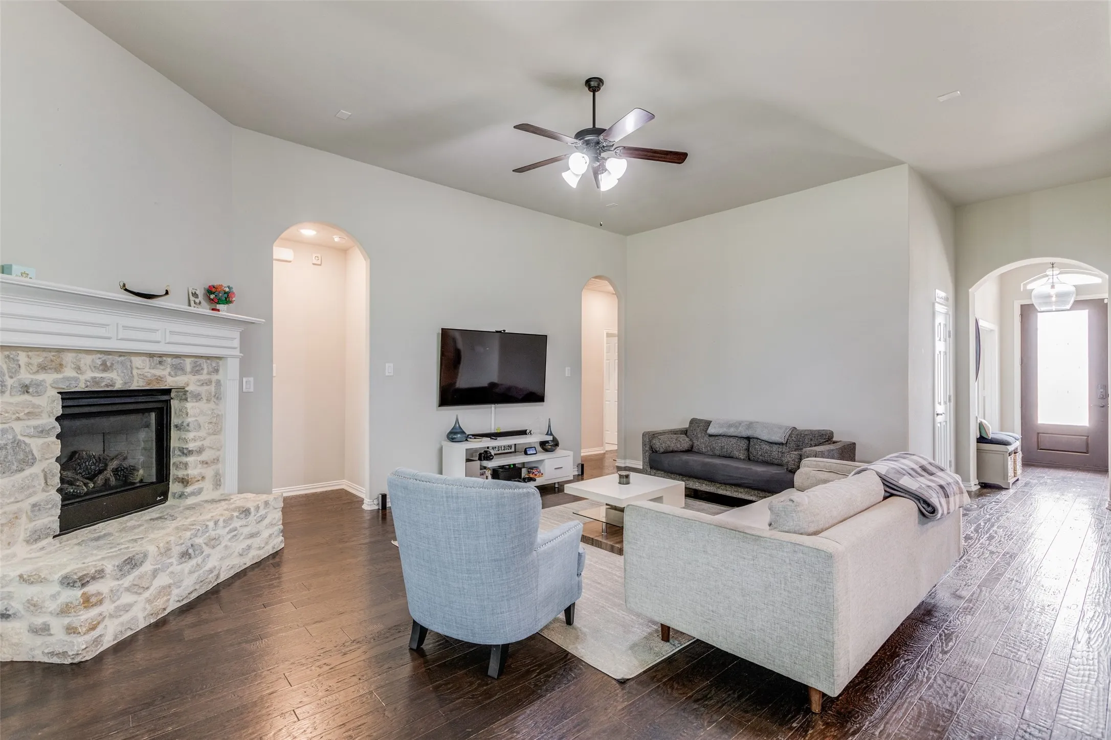 Spacious living area featuring high vaulted ceilings, stone fireplace, dark wood-finish flooring, and arched doorways