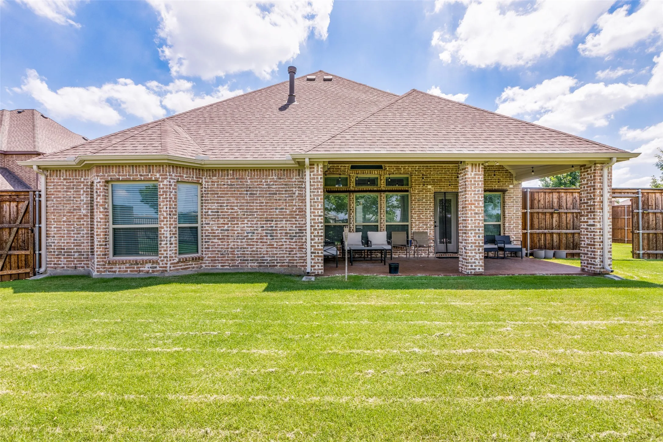 Brick exterior featuring a covered patio, multiple windows, and a shingle roof