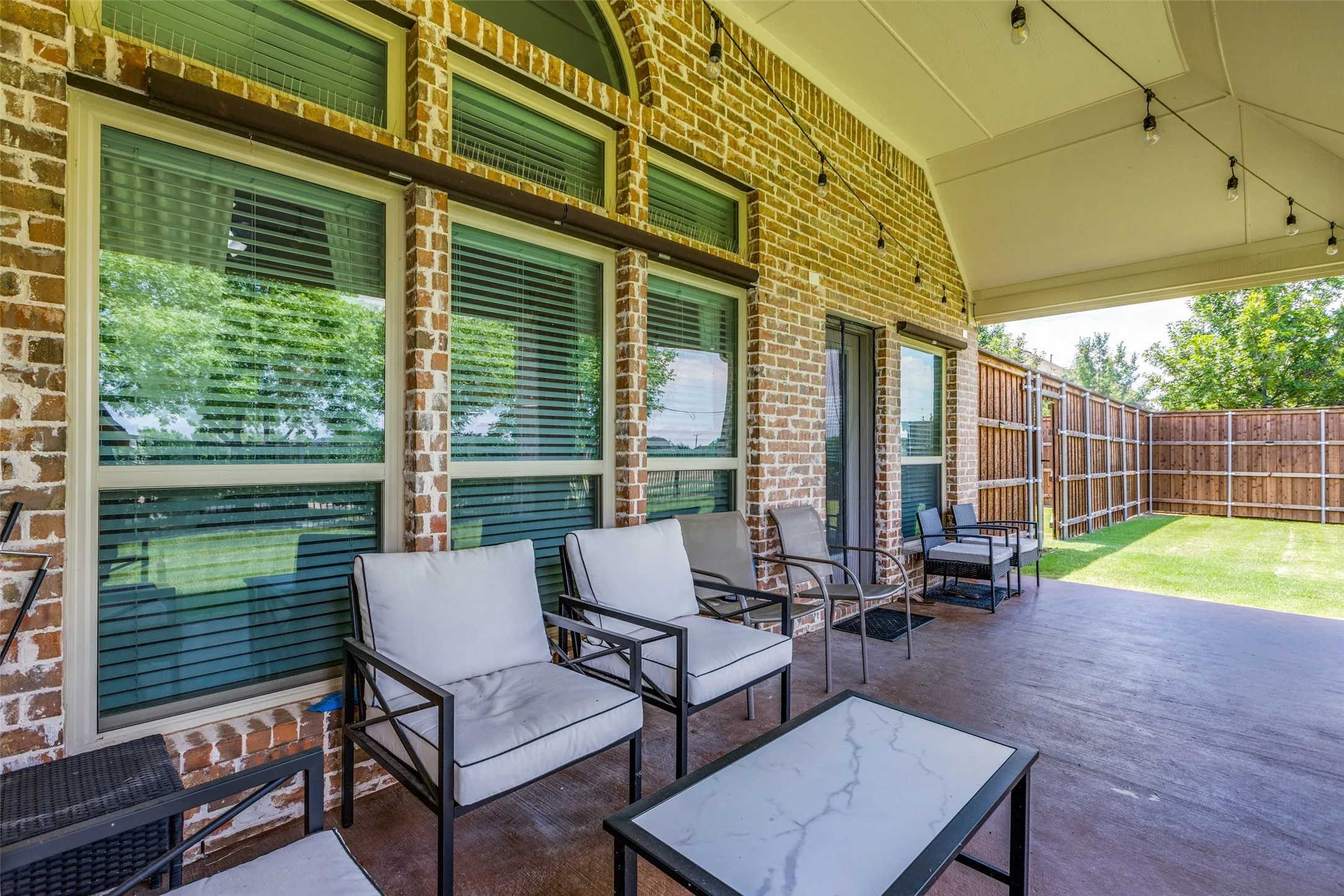 Covered patio with a stained concrete surface, brick exterior, string lighting, and a wood privacy fence