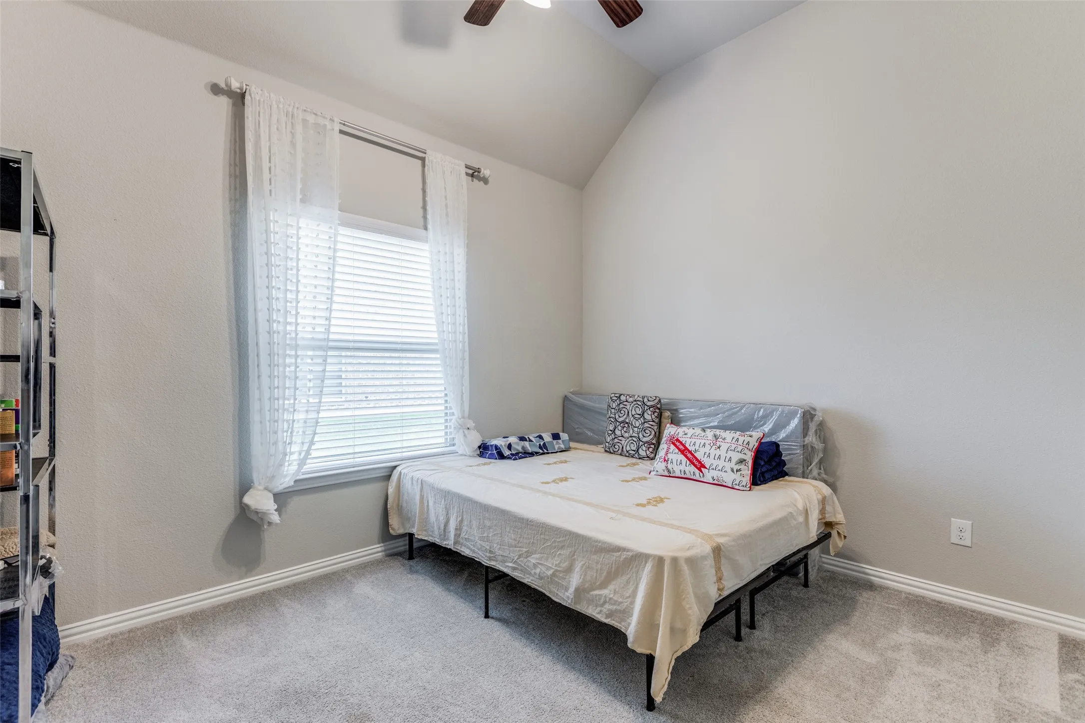 Vaulted ceiling, ceiling fan, window with blinds, carpet flooring, and neutral wall paint