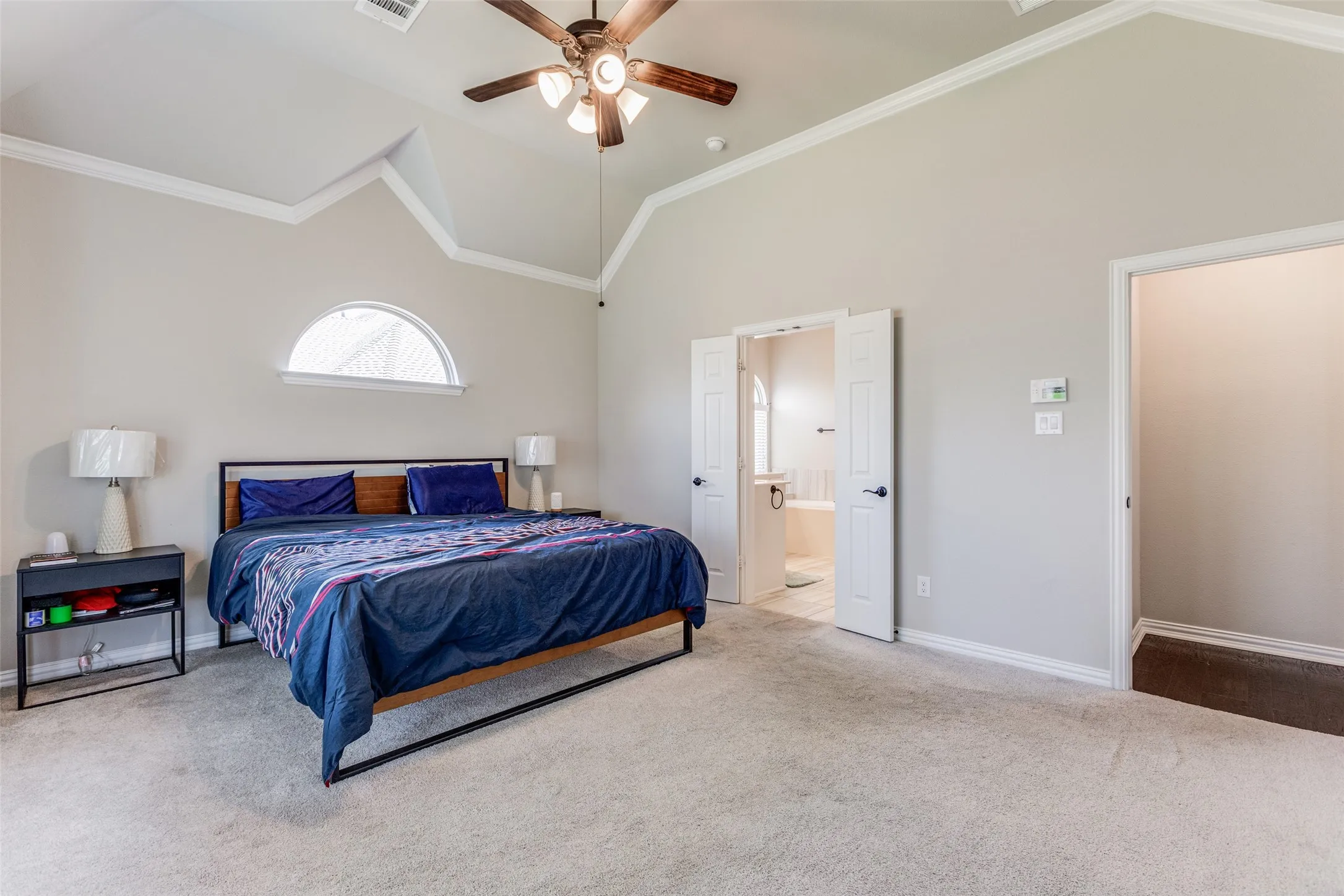 Vaulted ceiling with crown molding, ceiling fan, arched window, and carpet flooring
