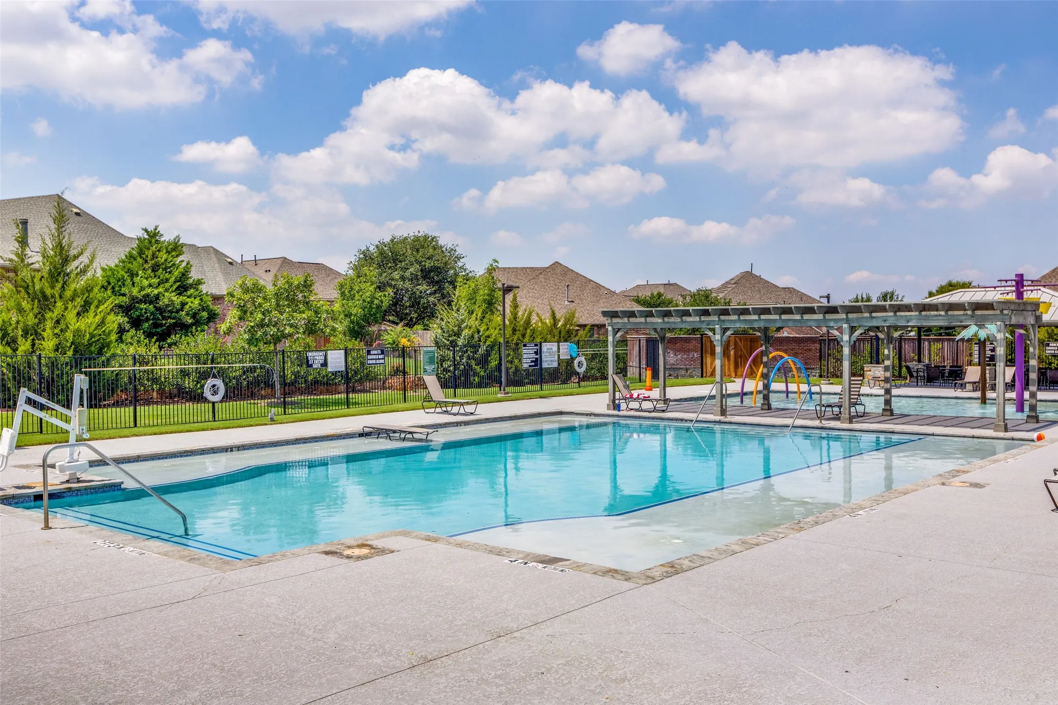 Resort-style pool with integrated splash pad, expansive concrete decking, and an adjacent shaded pergola
