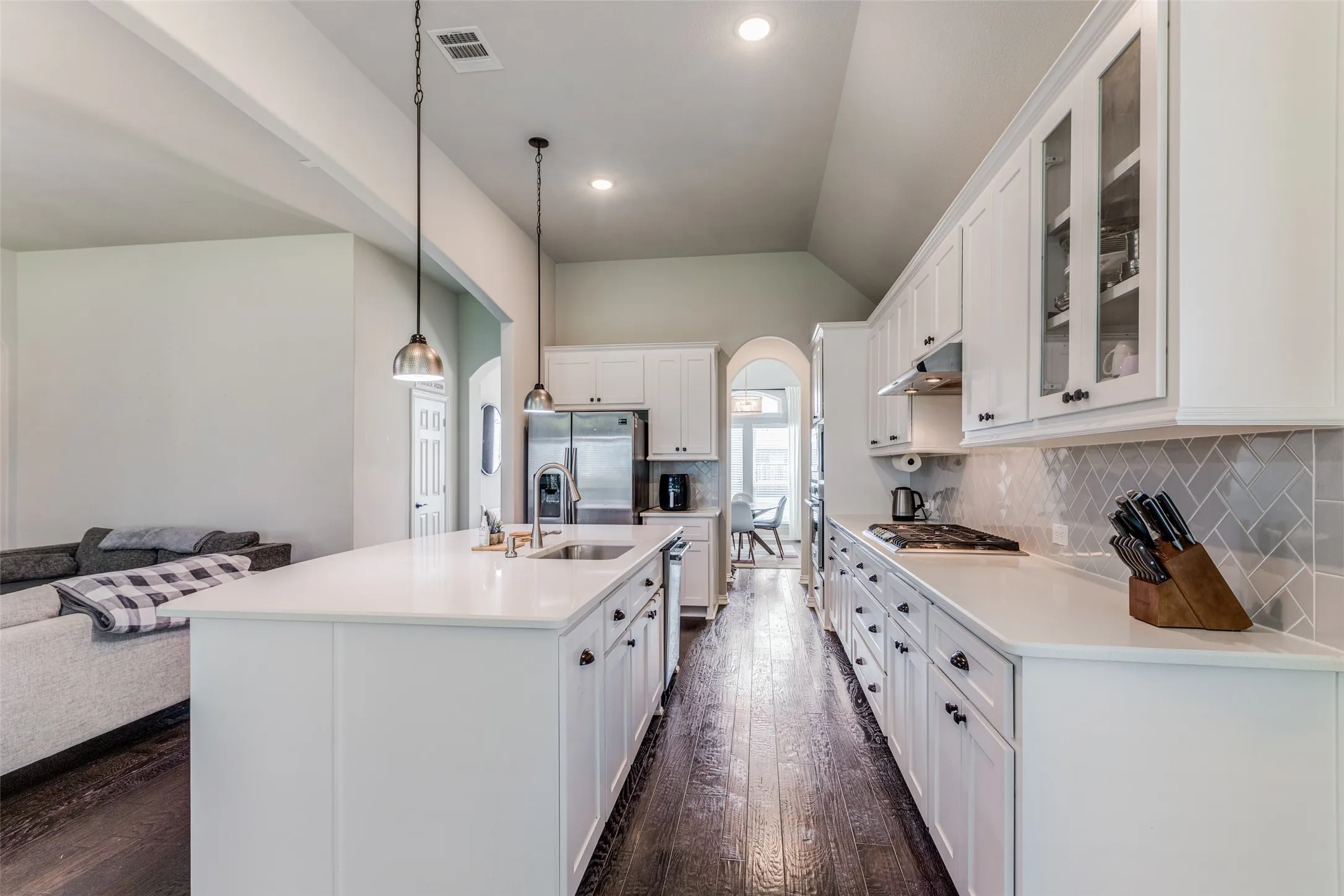 Kitchen featuring dark wood-finish flooring, white cabinetry, a large kitchen island with an undermount sink, and stainless steel appliances