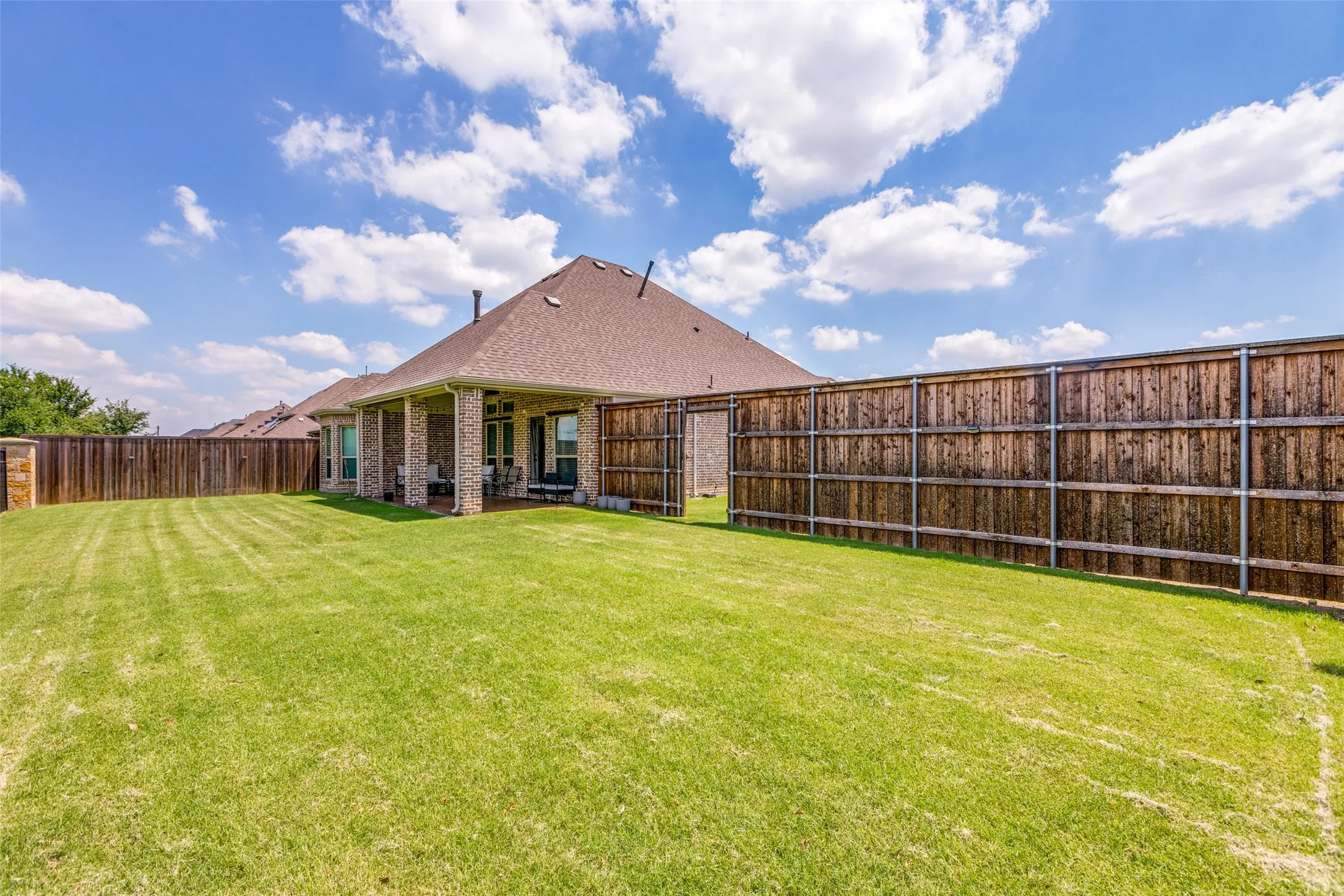 Expansive green lawn, wood privacy fencing, covered patio, brick exterior, and a shingle roof